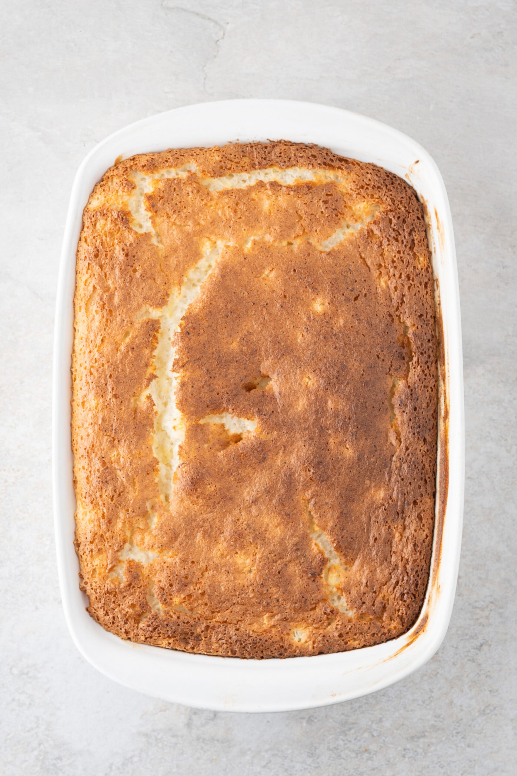 Fully baked pineapple angel food cake cooling in baking pan, top is golden brown
