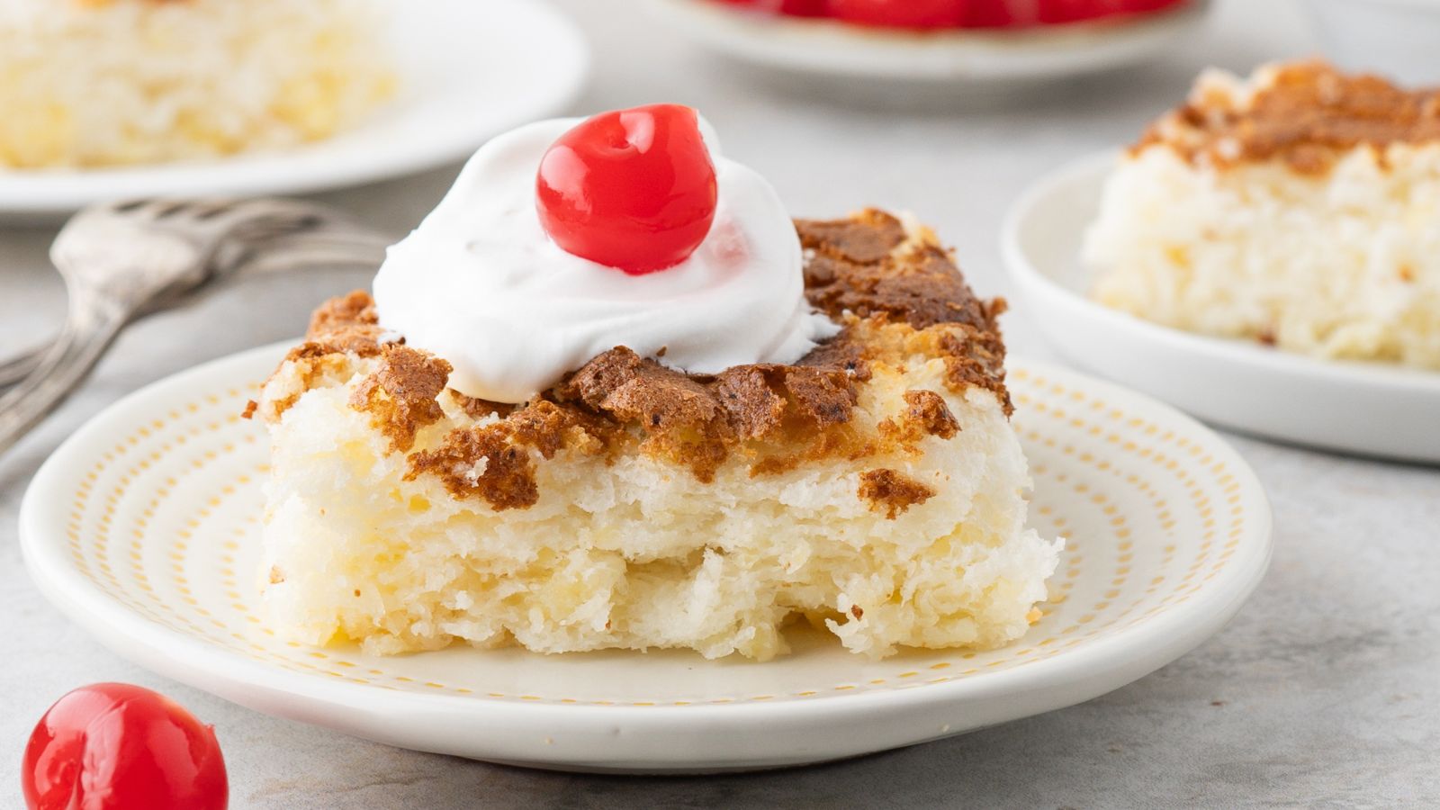 pineapple angel food cake square topped with whipped cream and a cherry on a white plate