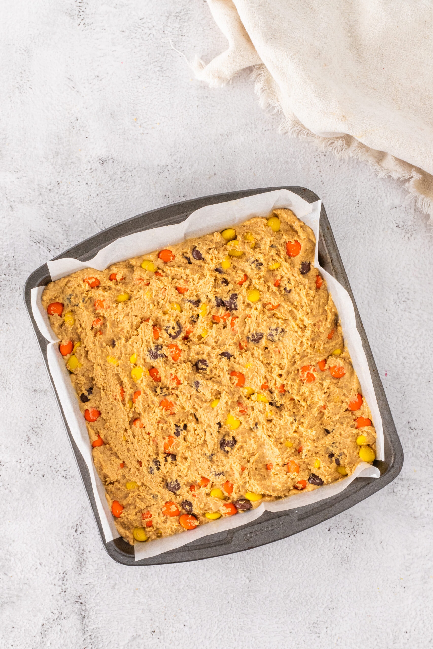 Pressing the dough with Reese's pb candy pieces into the prepared pan on top of the Reese's Peanut Butter Cups.