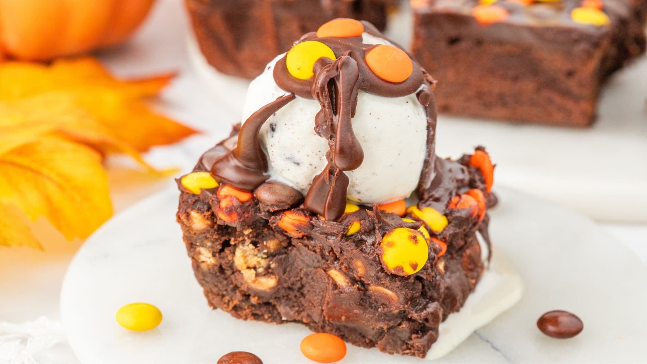 Reese's Pieces brownie close up. With ice cream scoop on top with melted chocolate drizzled on top