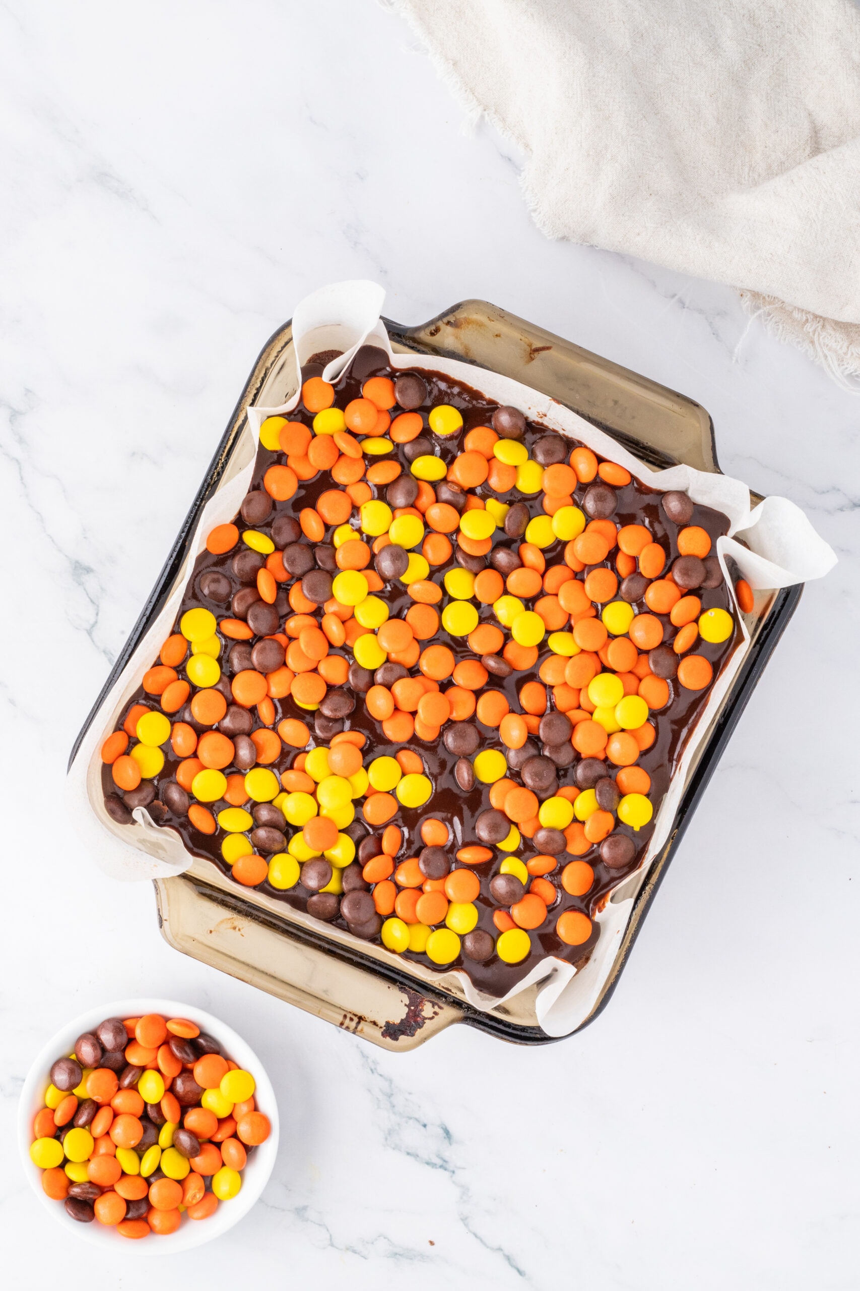 Reese's Pieces in pan, chocolate ganache is poured on top