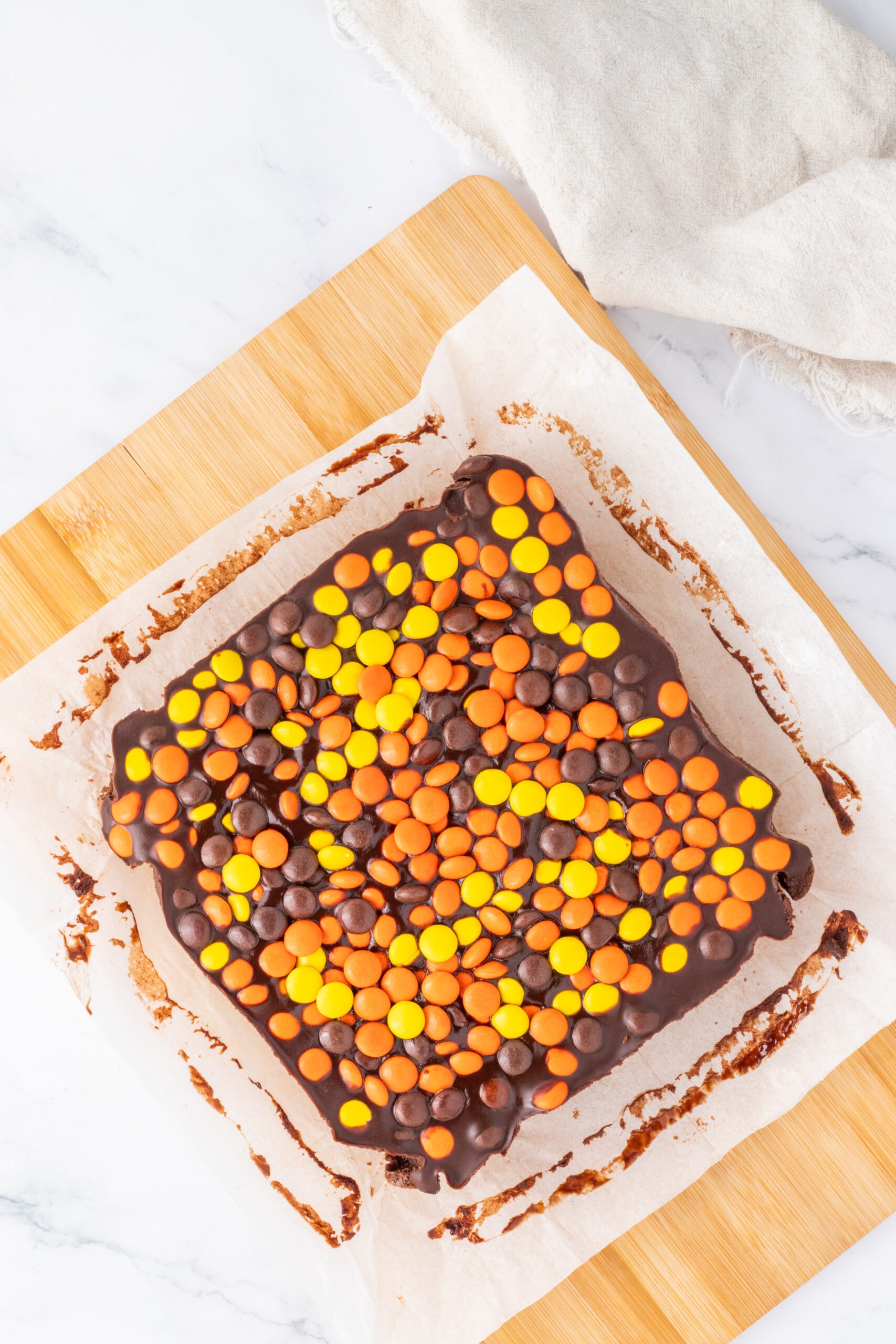Reese's Pieces pulled from the pan with parchment paper, ready to be cut into squares.