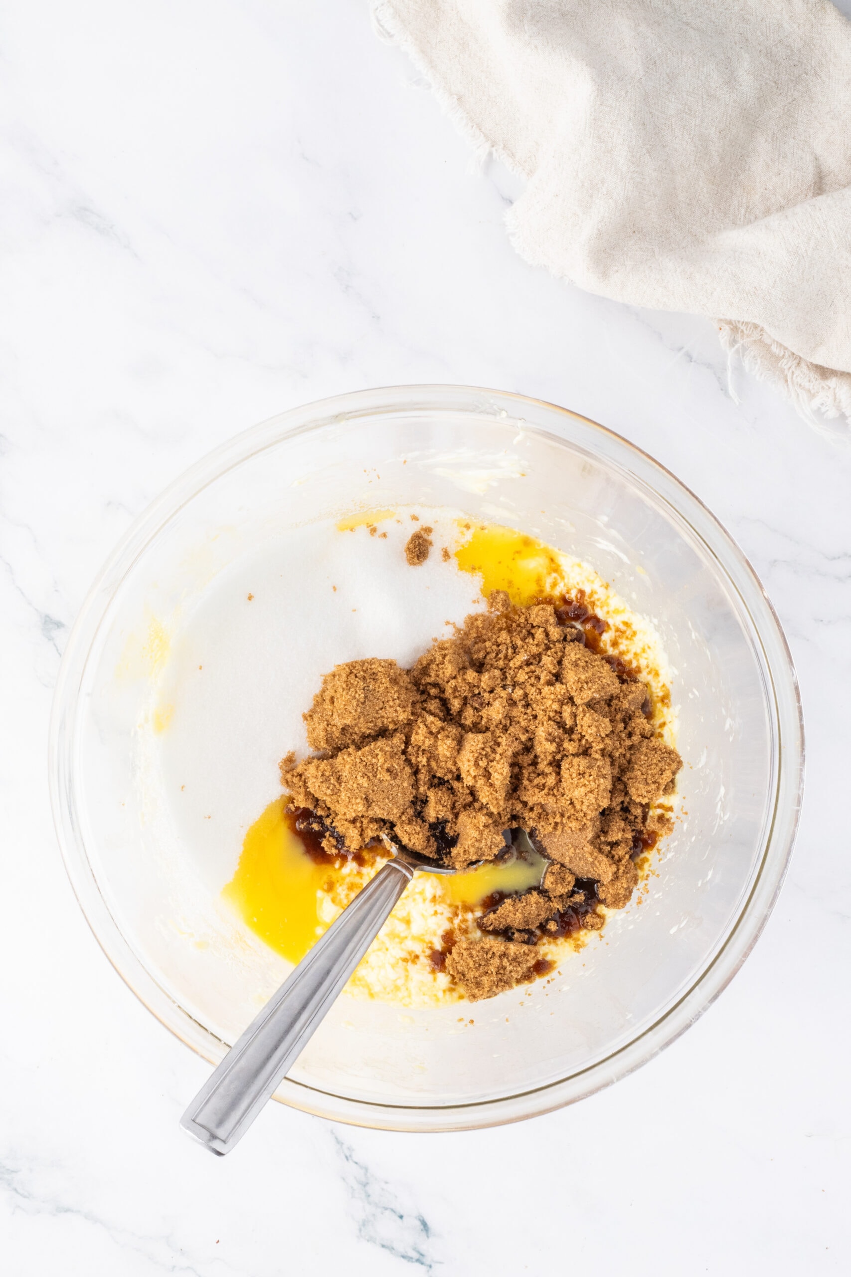 Adding the white and brown sugars, softened butter, egg plus yolk, and vanilla bean past to a bowl to create the batter.