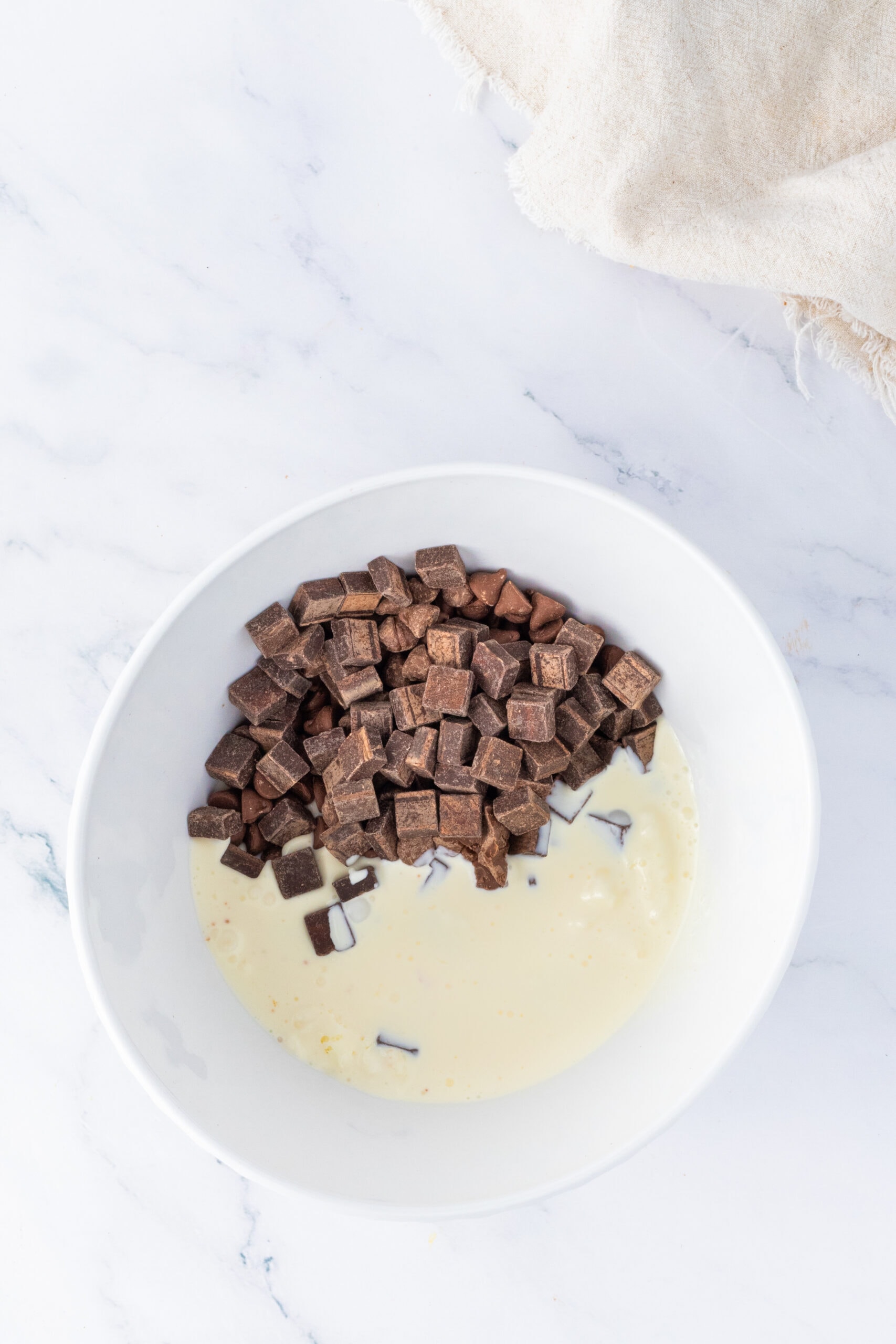 Chocolate chips are in a bowl with heavy cream, ready to be melted together to create ganache
