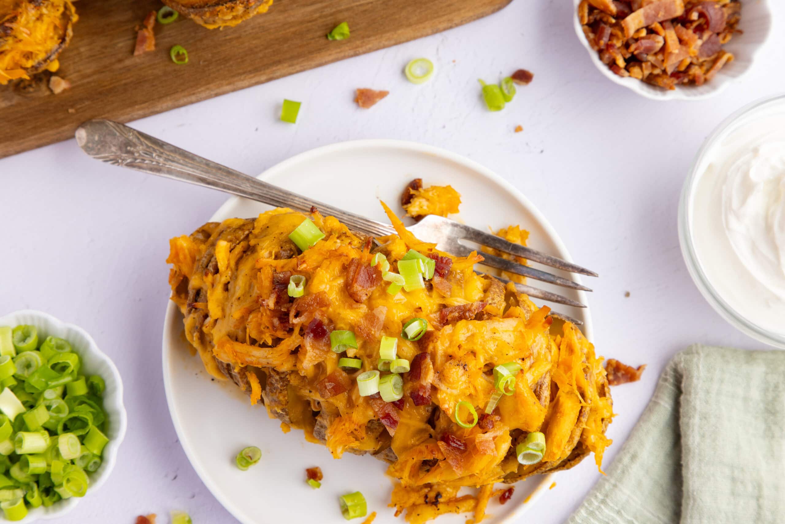 Stuffed potato on a plate, topped with green onion and bacon.