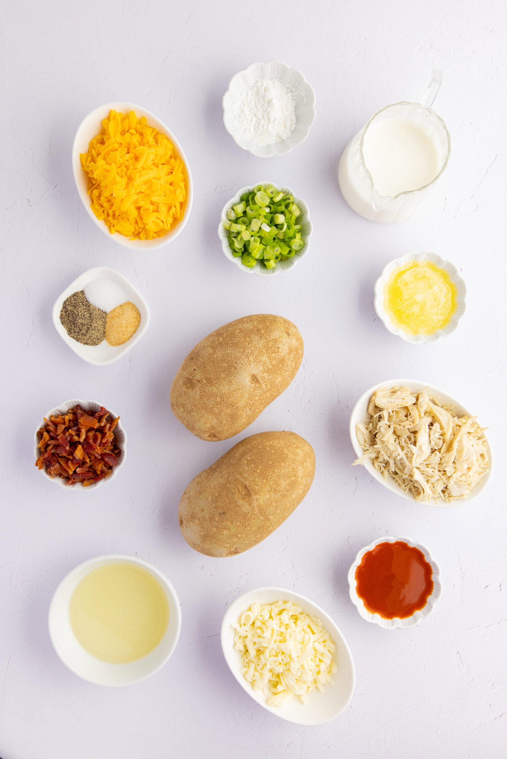 All ingredients pictured: cheddar and mozzarella cheese, oil, salt and pepper, hot sauce, potatoes, bacon, cornstarch, chives, garlic powder, butter, shredded chicken.