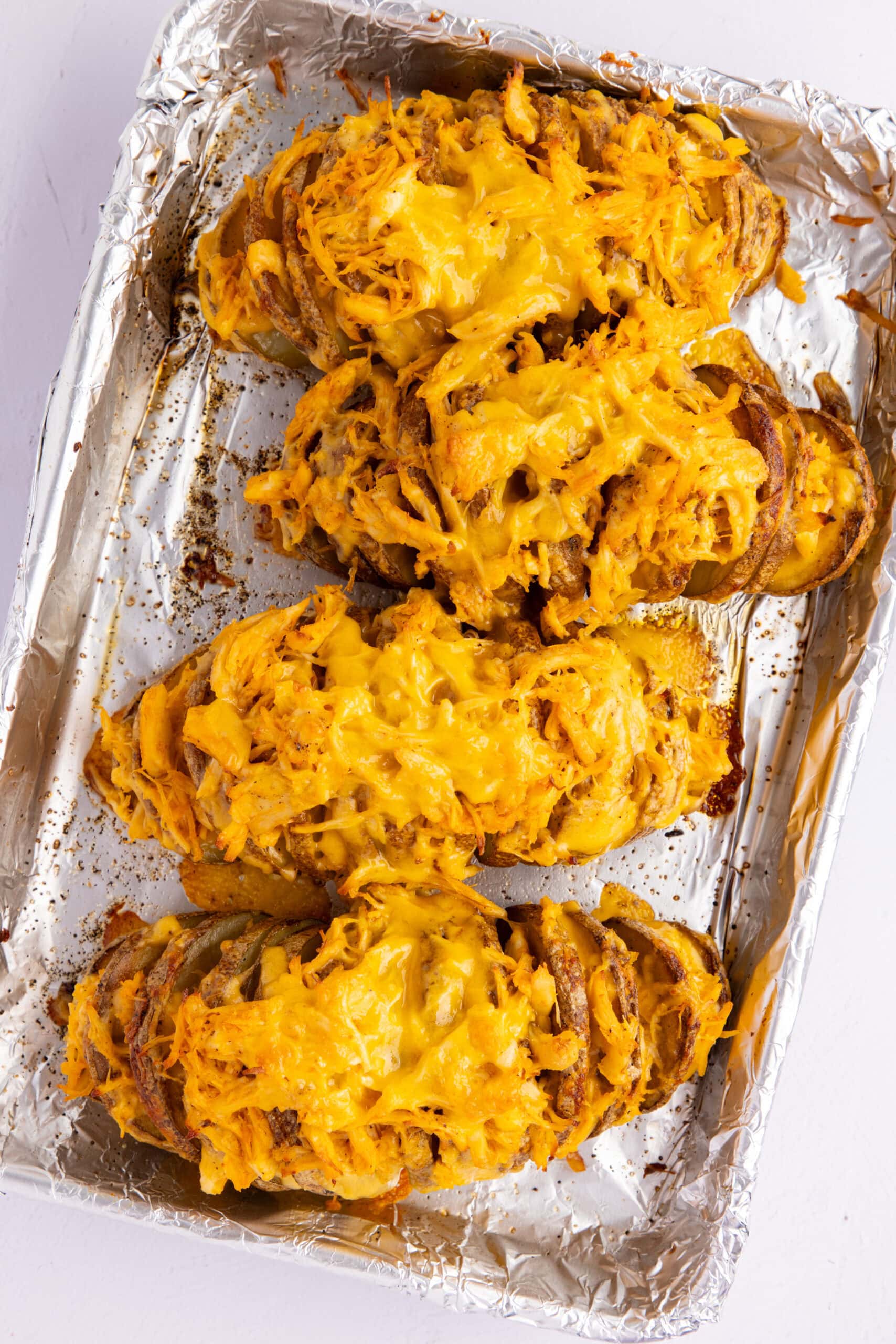 Cheese is all melted on top of shredded chicken on stuffed potatoes on a baking sheet