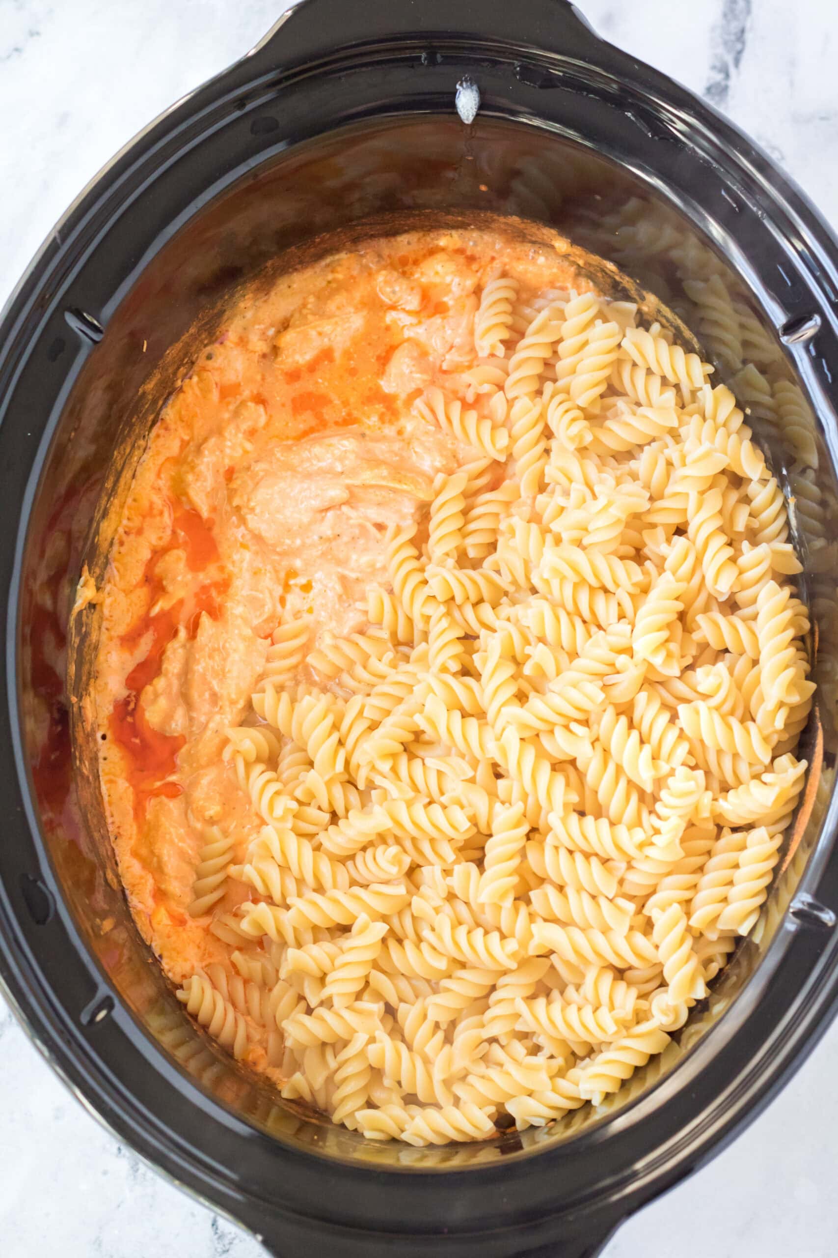 Adding pasta to the chicken buffalo mixture in the crockpot
