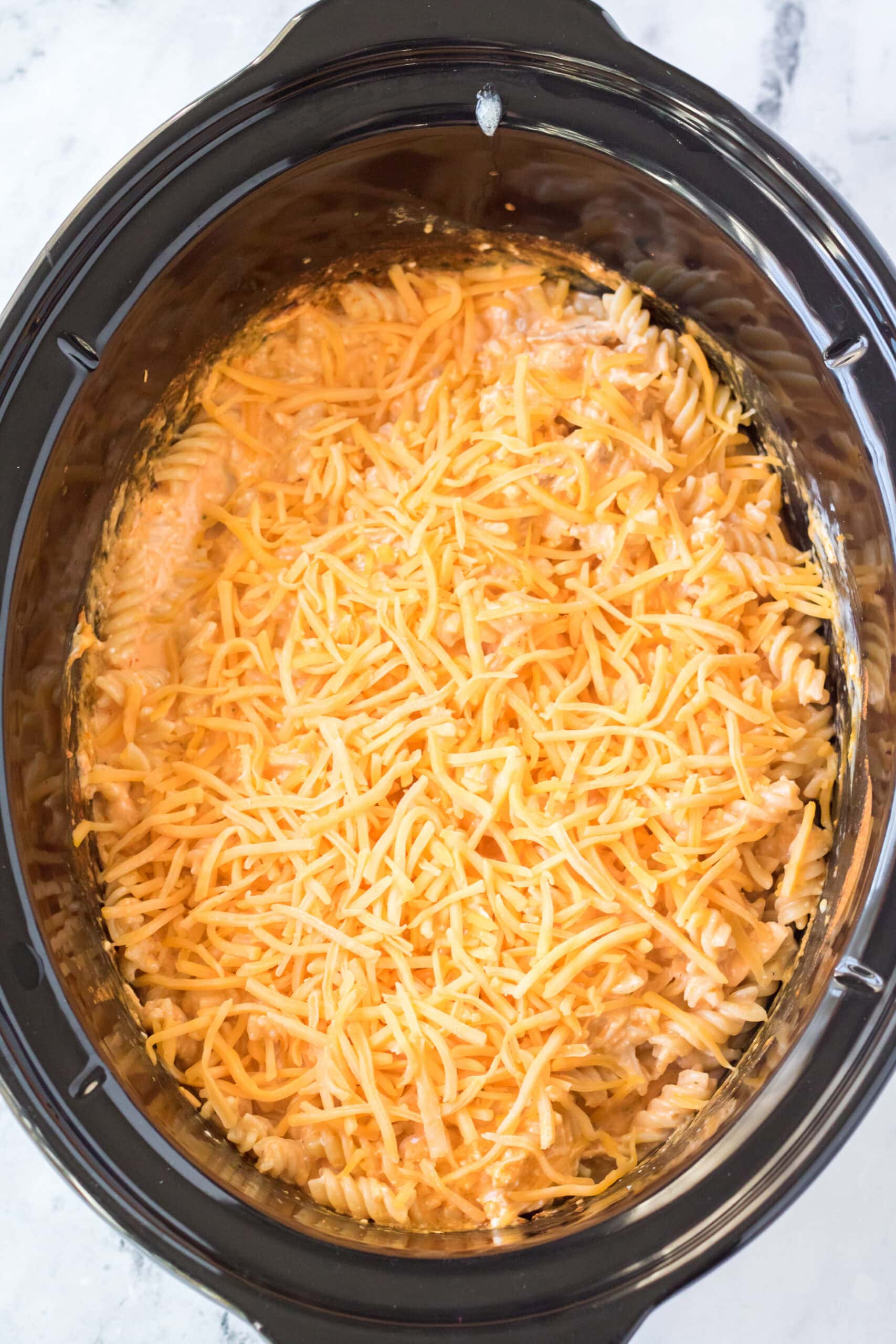 Adding shredded cheddar cheese on top of chicken and pasta in crockpot