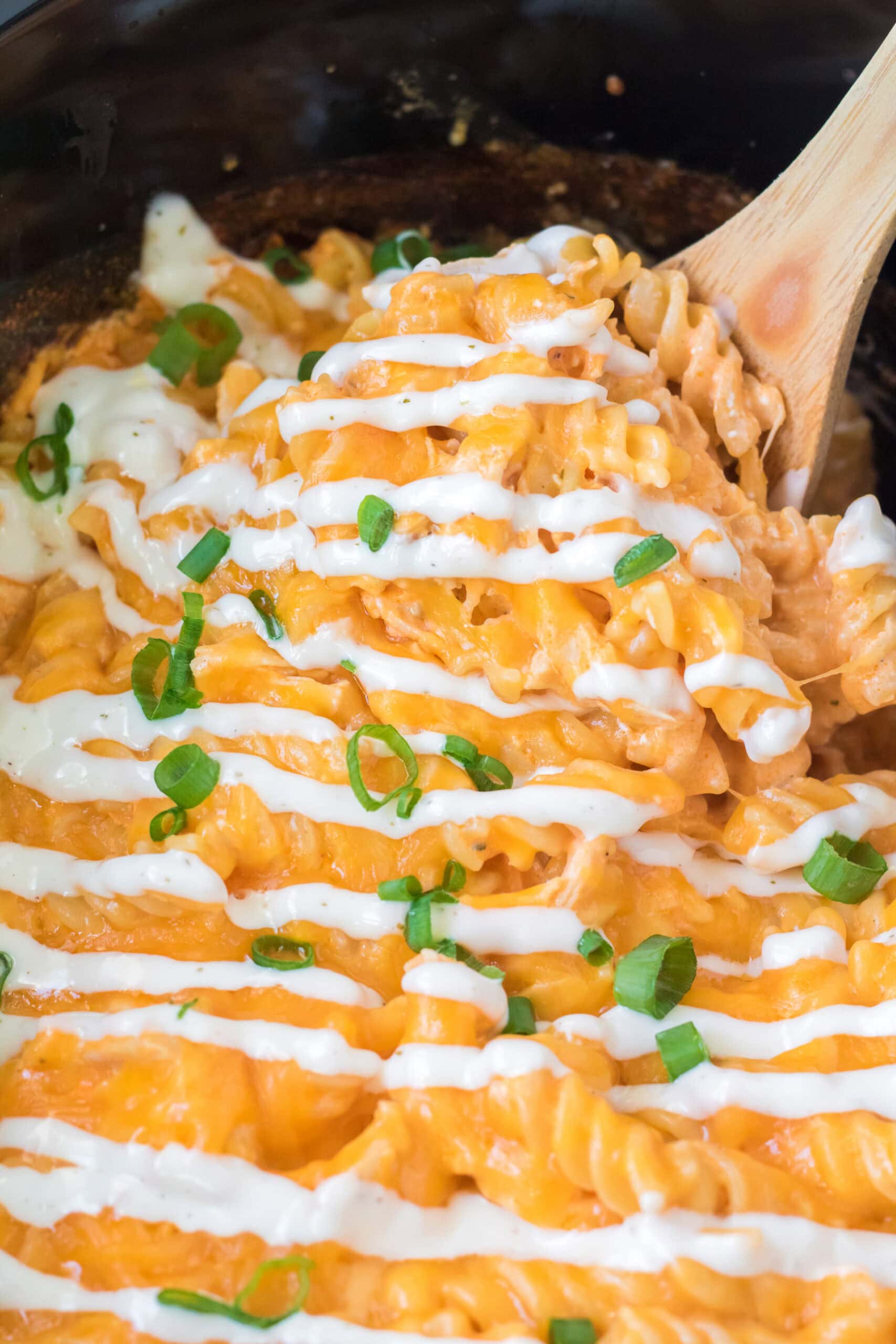 Up close buffalo chicken dip in crockpot, ranch drizzle and green onions on top