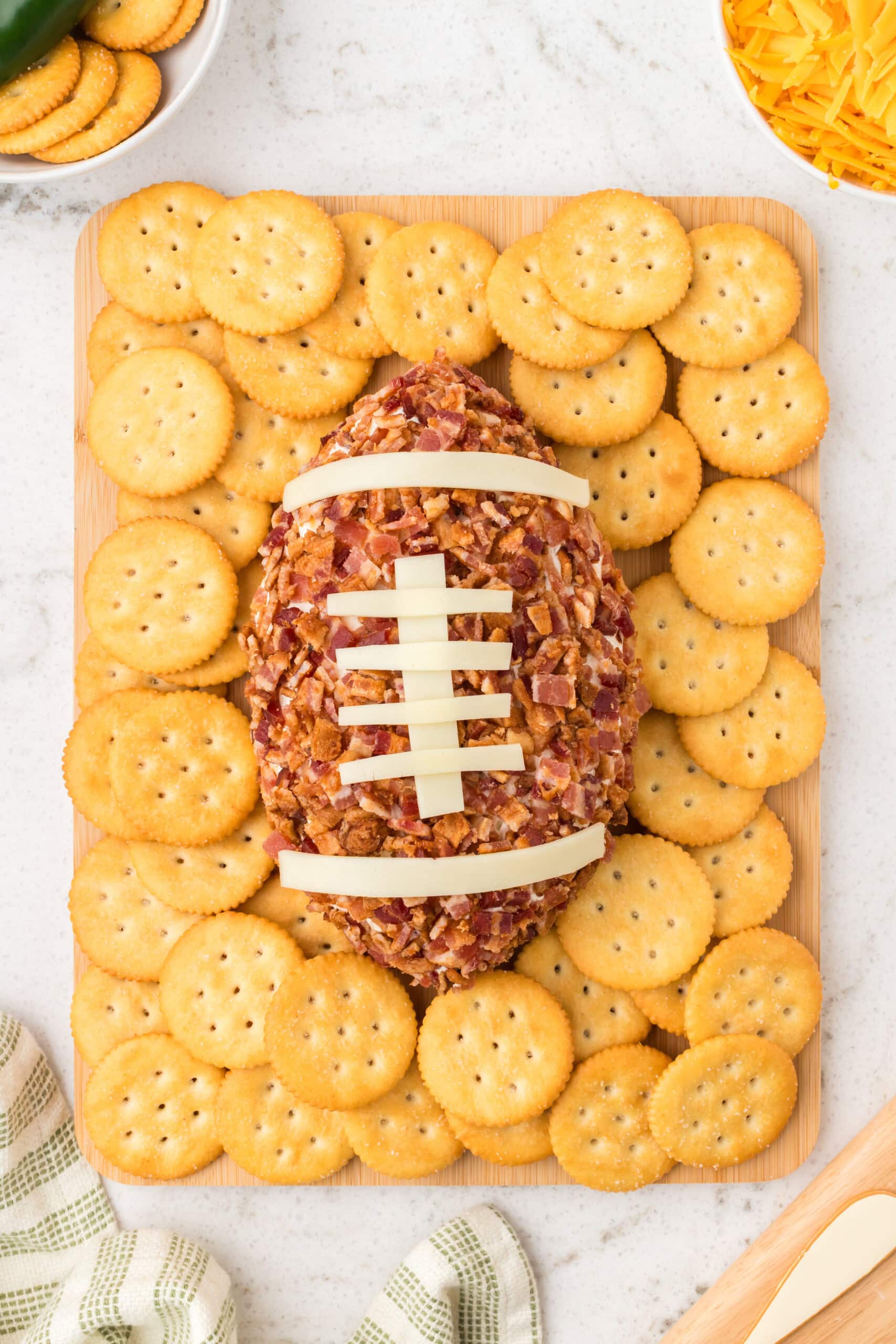 The football cheeseball is on a wood board surrounded by crackers, ready to be enjoyed