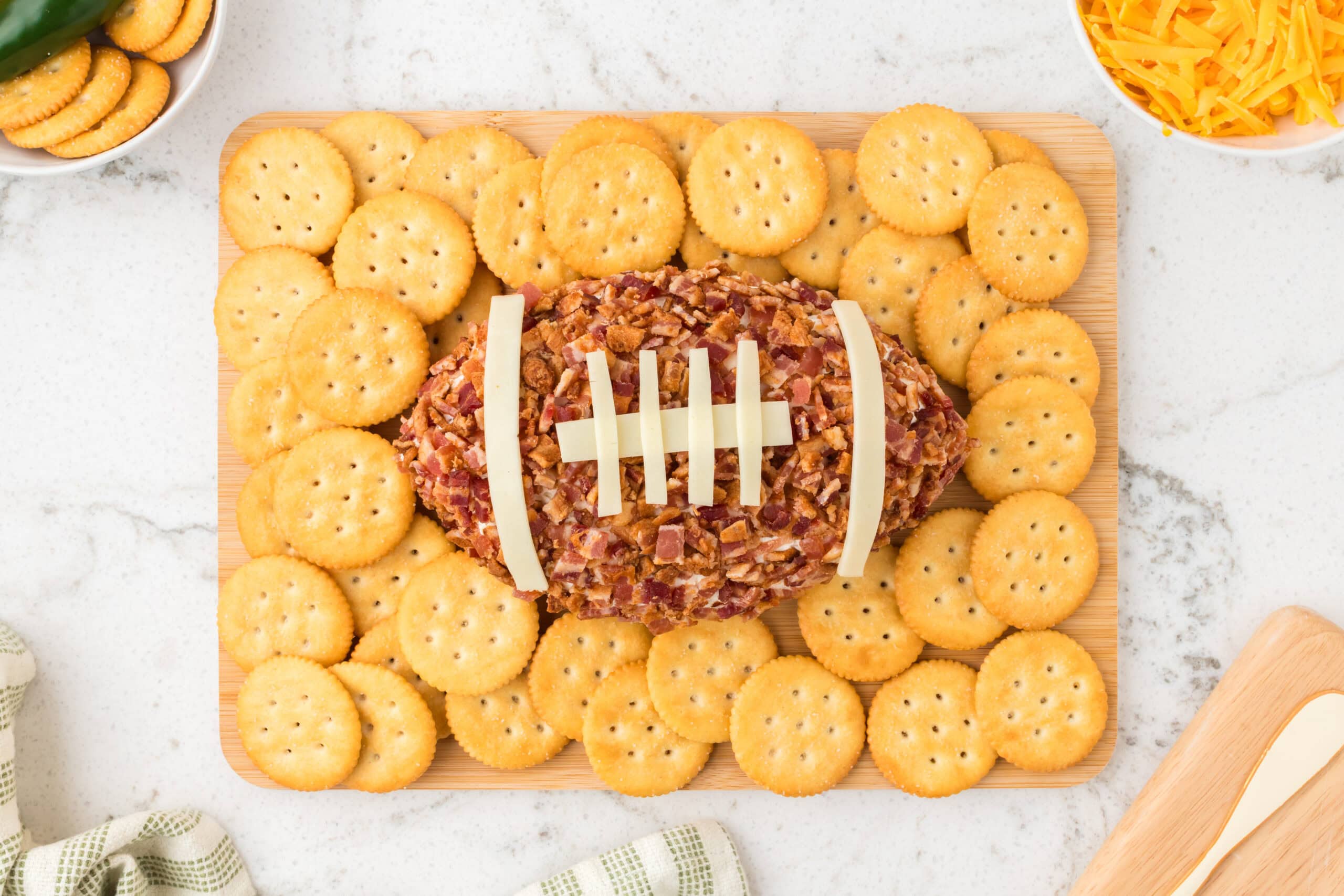 Jalapeno football cheeseball is on a wooden board, crackers all around, chilled and ready to be enjoyed