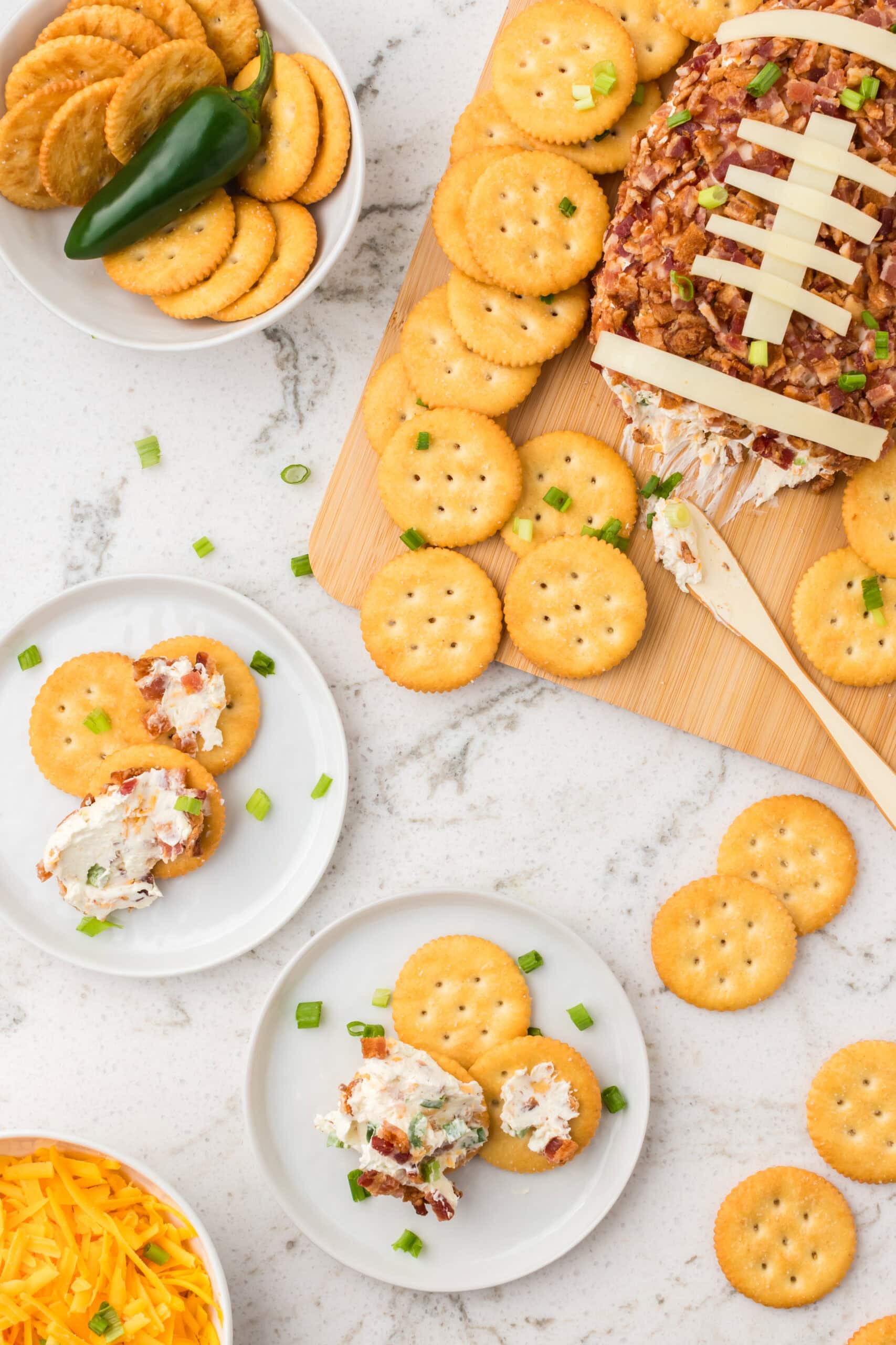 Football cheeseball is served on crackers on several plates.