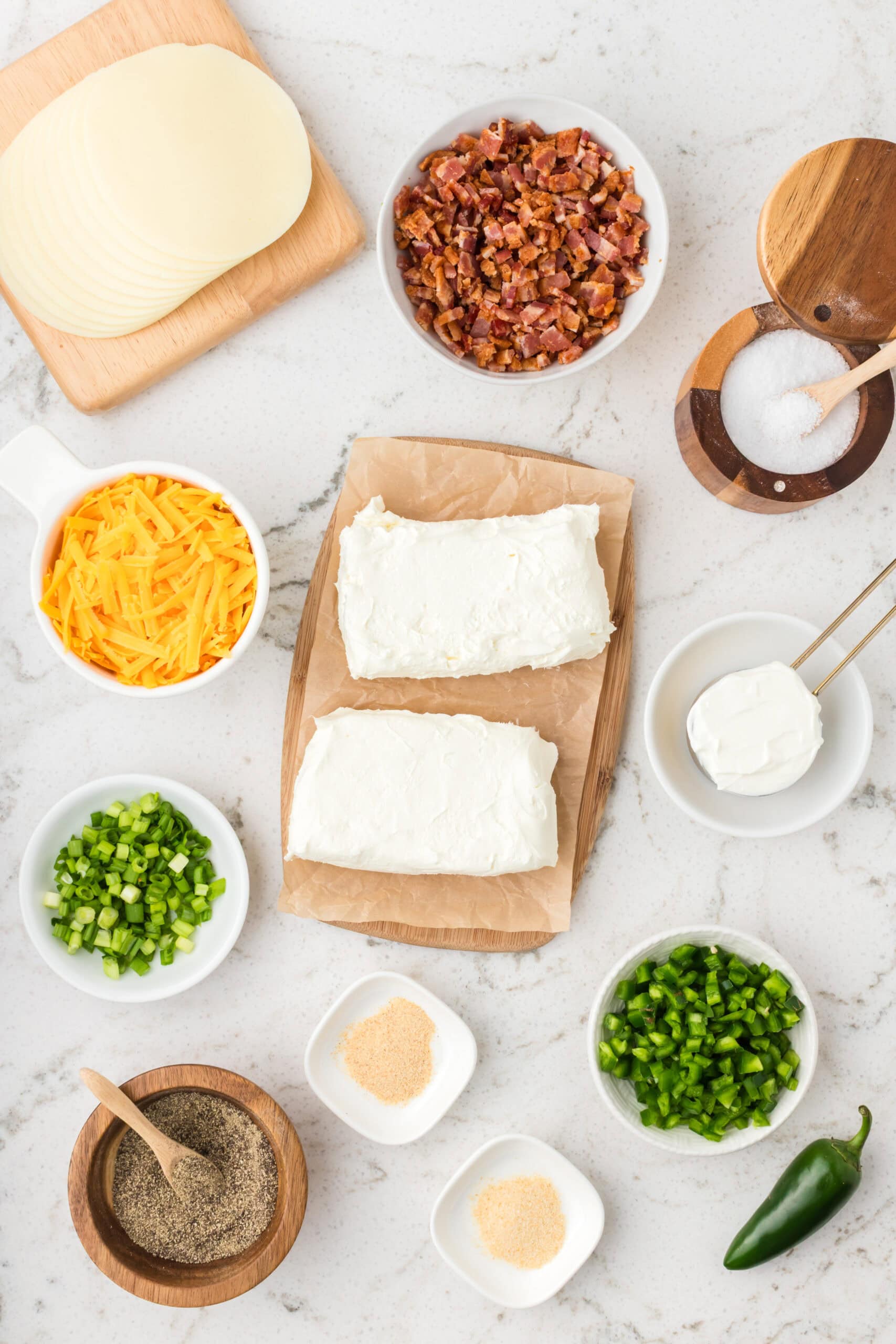 All ingredients pictured to make the jalapeno cheeseball: black pepper, salt, onion and garlic powder, cream cheese, sour cream, bacon, green onions, and provolone cheese.