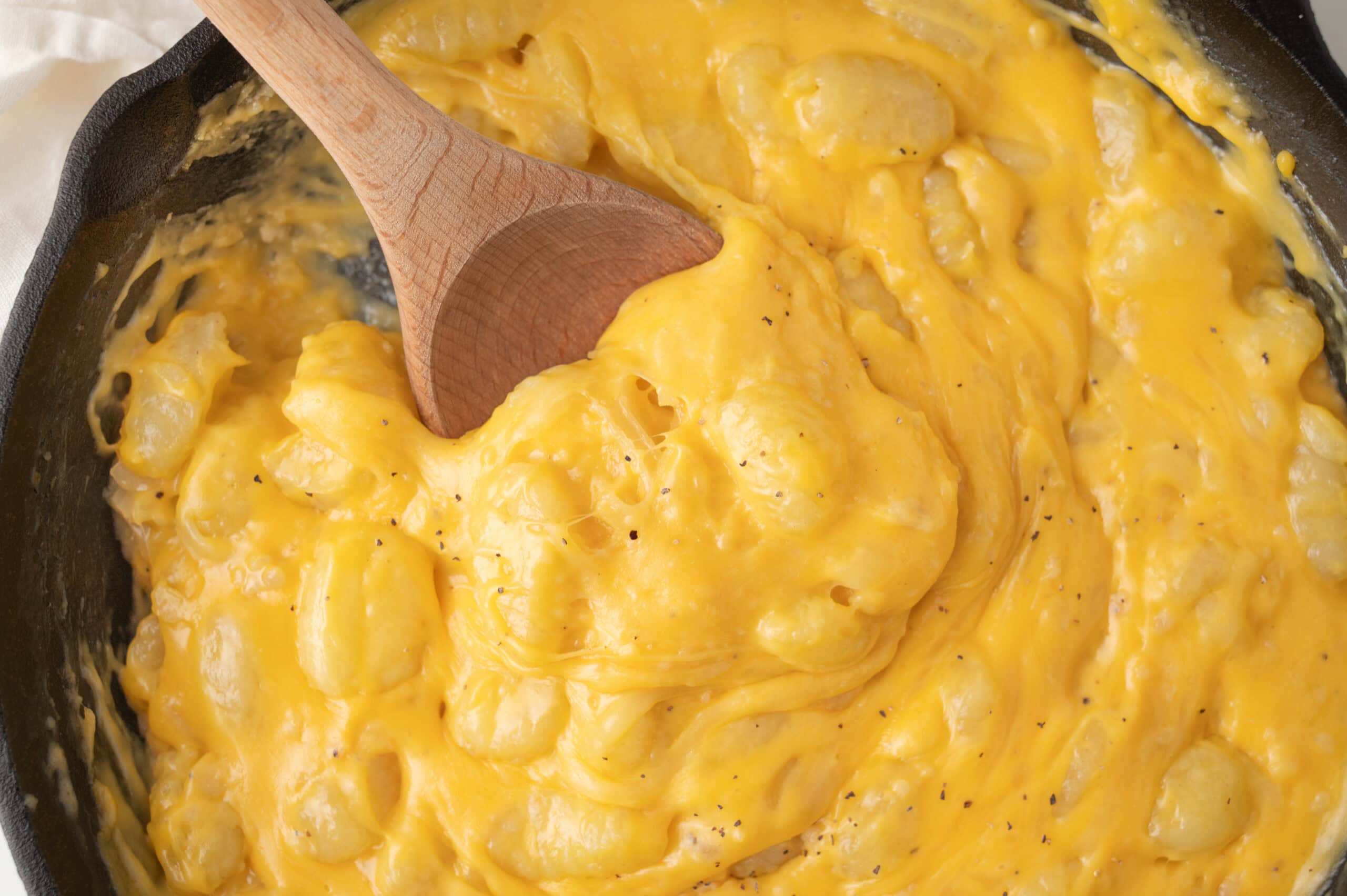 Gnocchi mac and cheese being scooped up in the baking pan with a wooden spoon