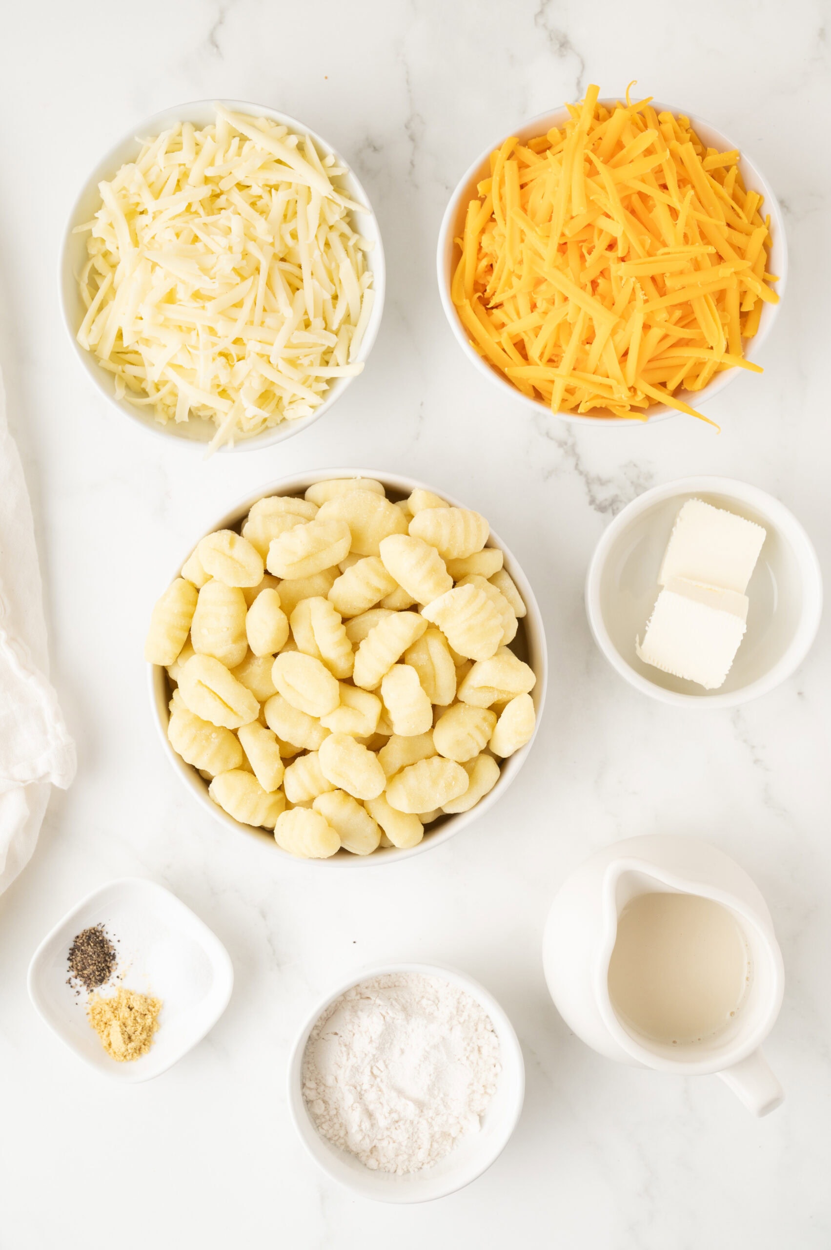 All ingredients pictured: flour, gnocchi, butter, milk, mustard powder, salt, pepper, shredded cheddar cheese, mozzarella cheese