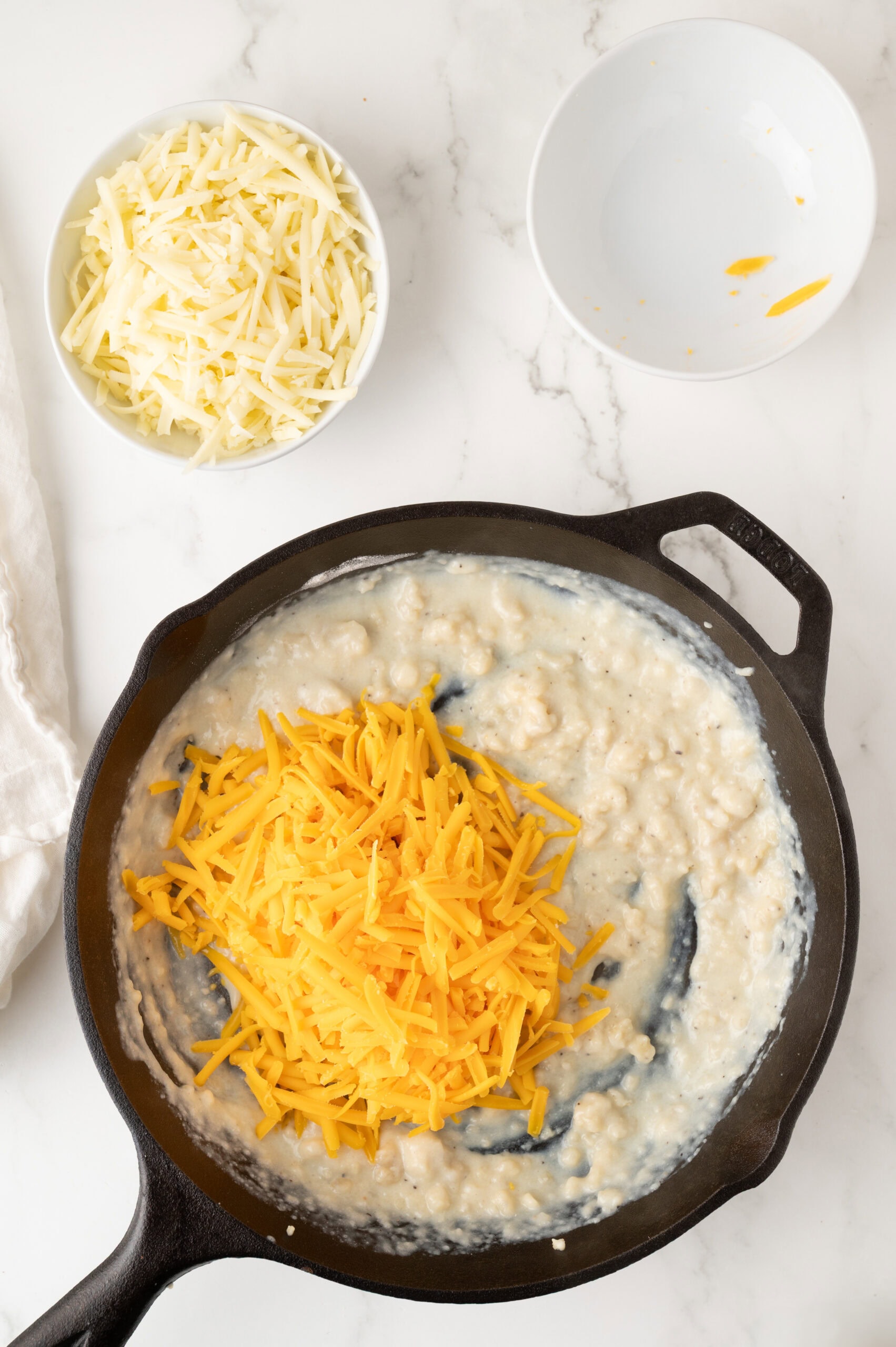 Adding shredded cheddar cheese to the roux in the cast iron pan