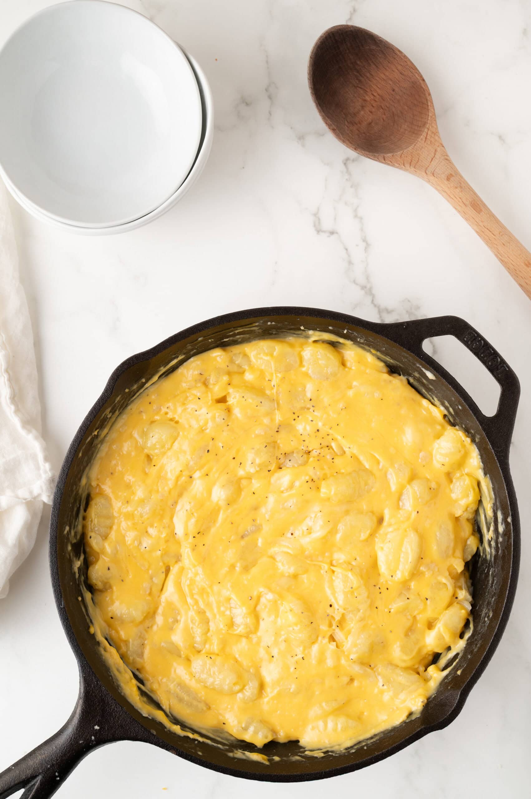 Adding cheese to the cast iron skillet to melt on top of gnocchi.