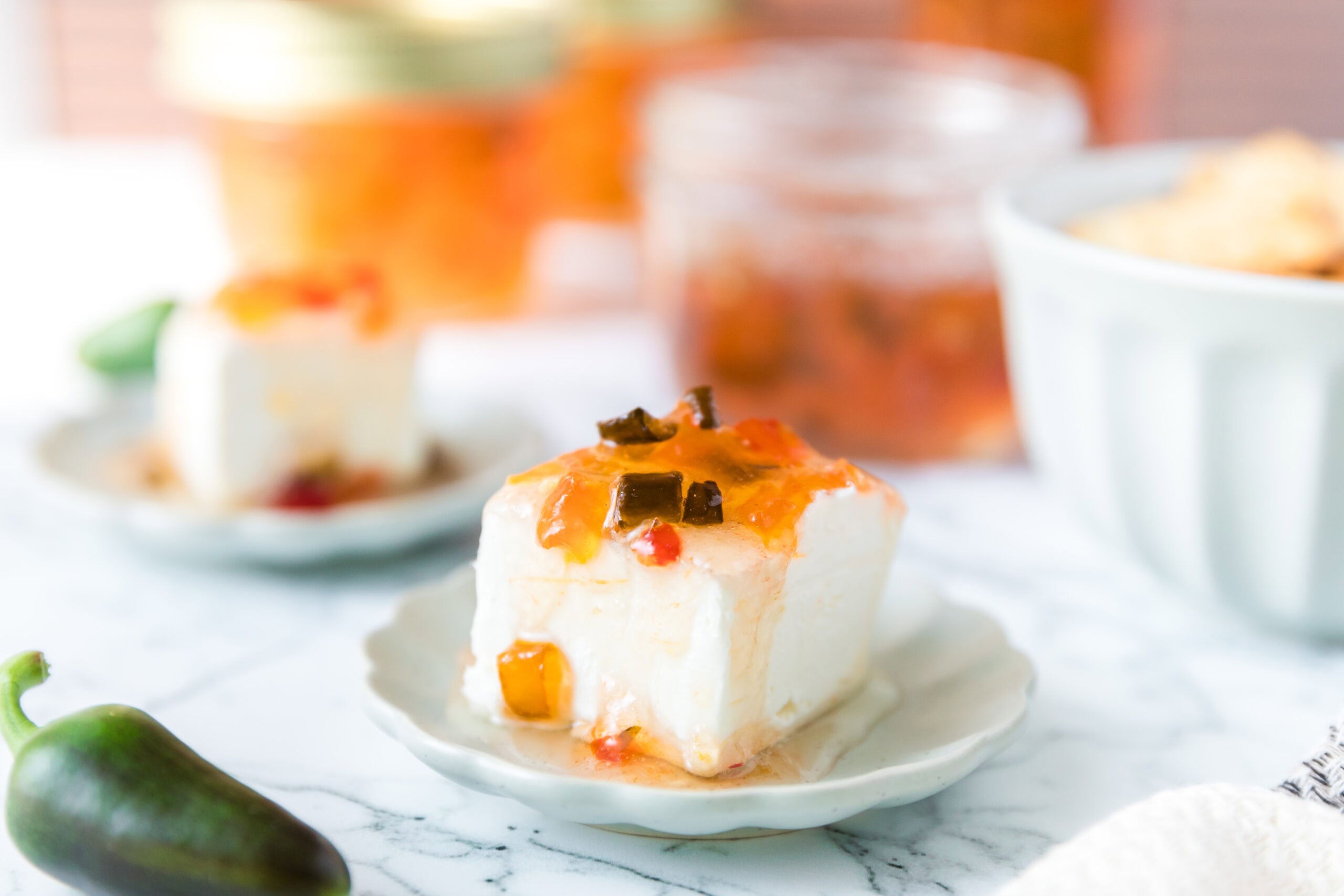Hot pepper jelly topped on a square piece of cream cheese on a small plate