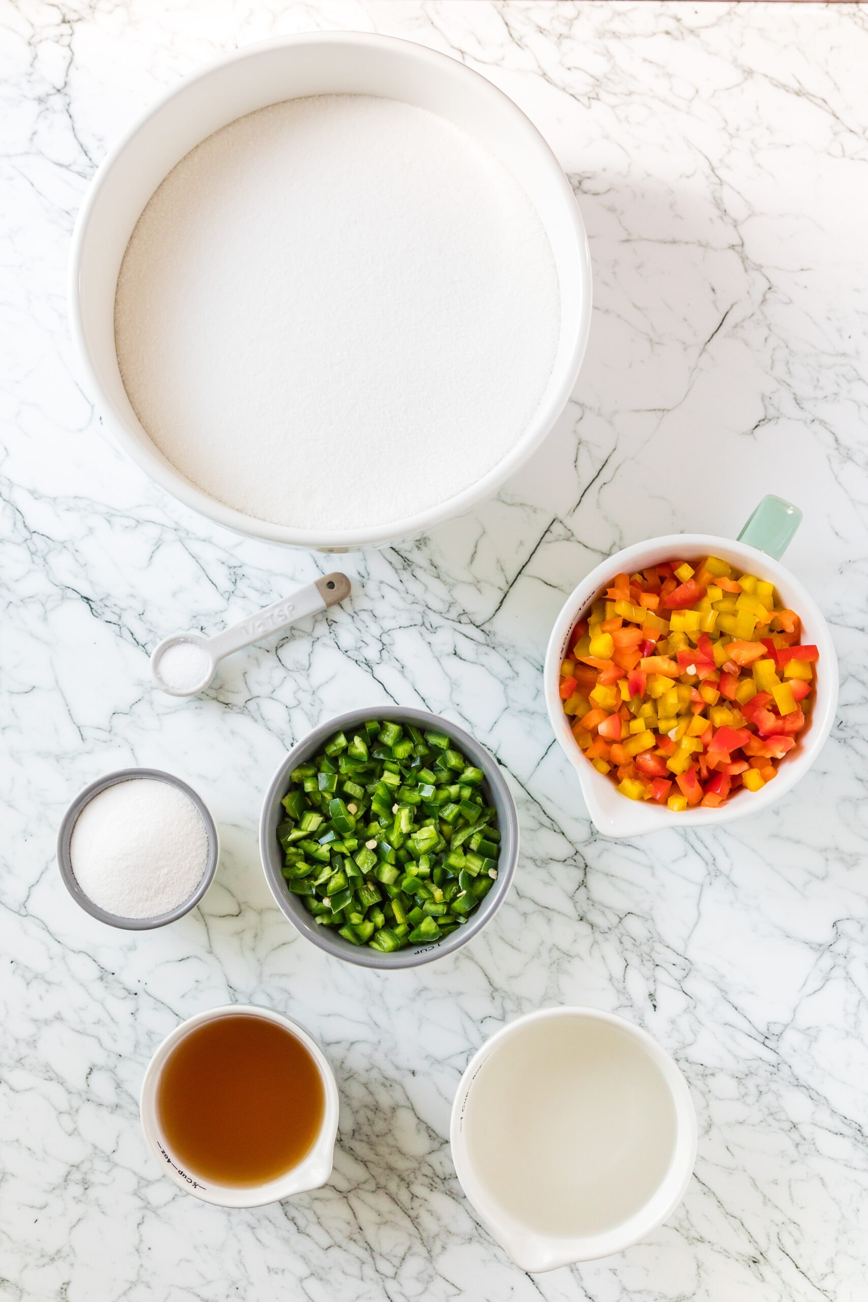 All ingredients to create hot pepper jelly: powder pectin, apple cider vinegar, white vinegar, bell pepper, sugar, salt, jalapenos.