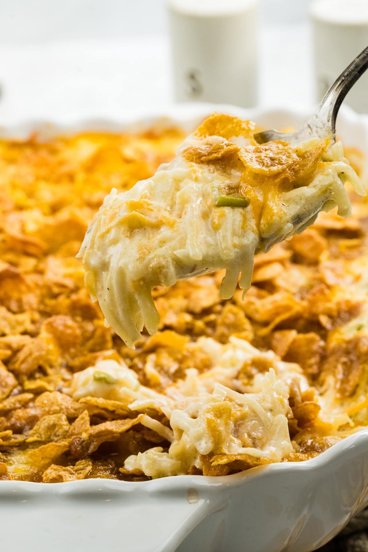 Cheesy potatoes are cooled and ready to be enjoyed. There is a scoop of the potatoes being lifted up