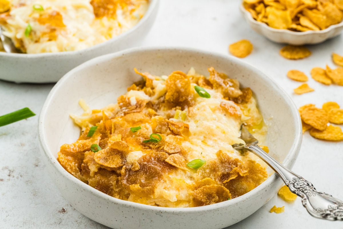 A bowl filled with cheesy potatoes topped with added green onions. A spoon is in the bowl.
