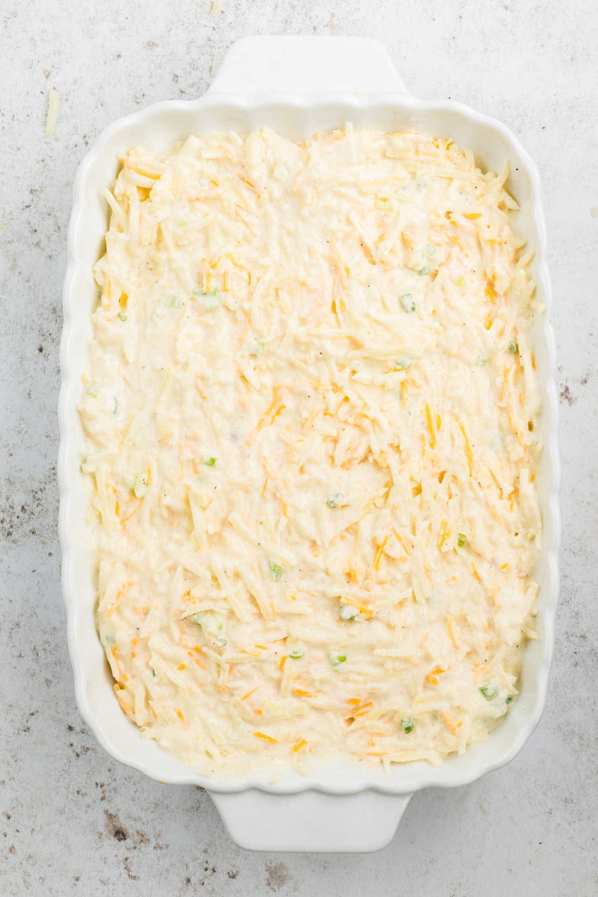 Adding thawed hash browns, cheddar cheese and green onion in a baking dish