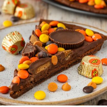 A slice of peanut butter pizza on a plate, Reese's pieces are scattered all around