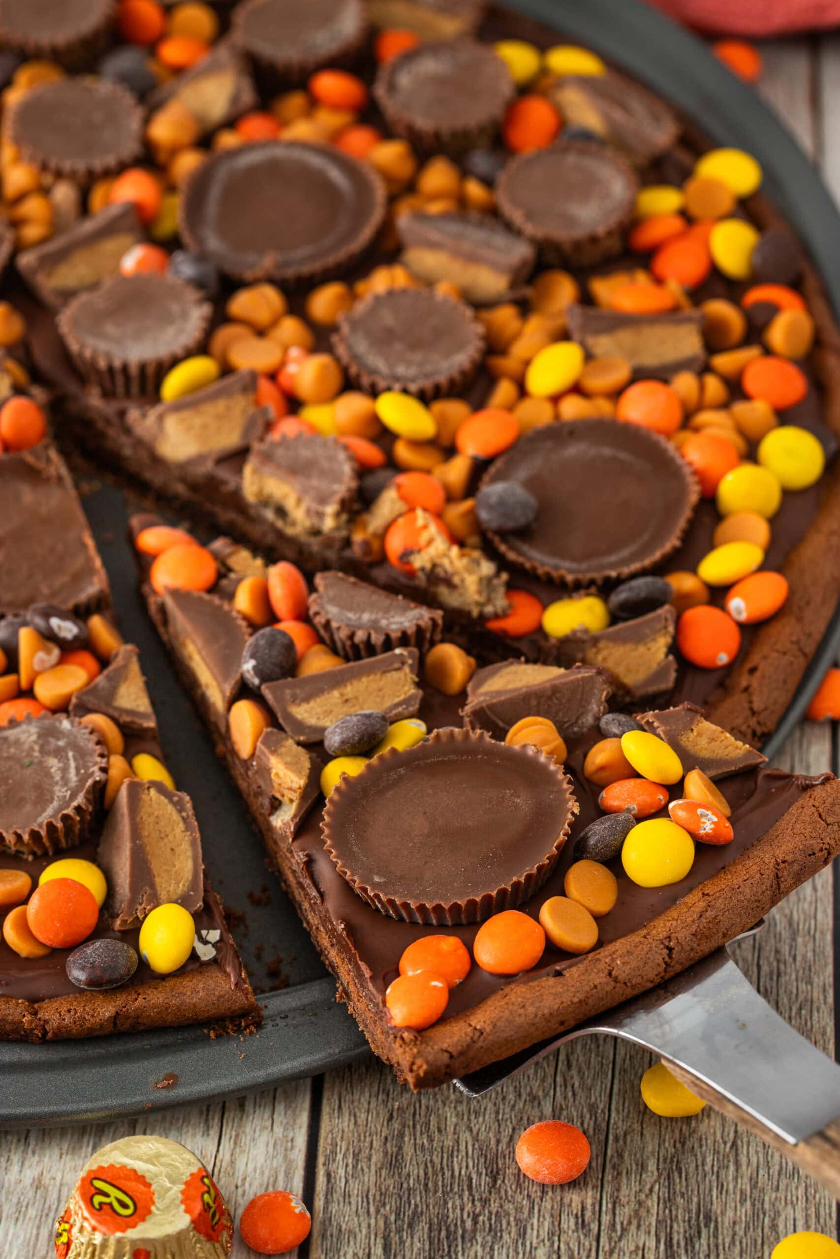 A slice cut into the peanut butter pizza and being pulled out to serve