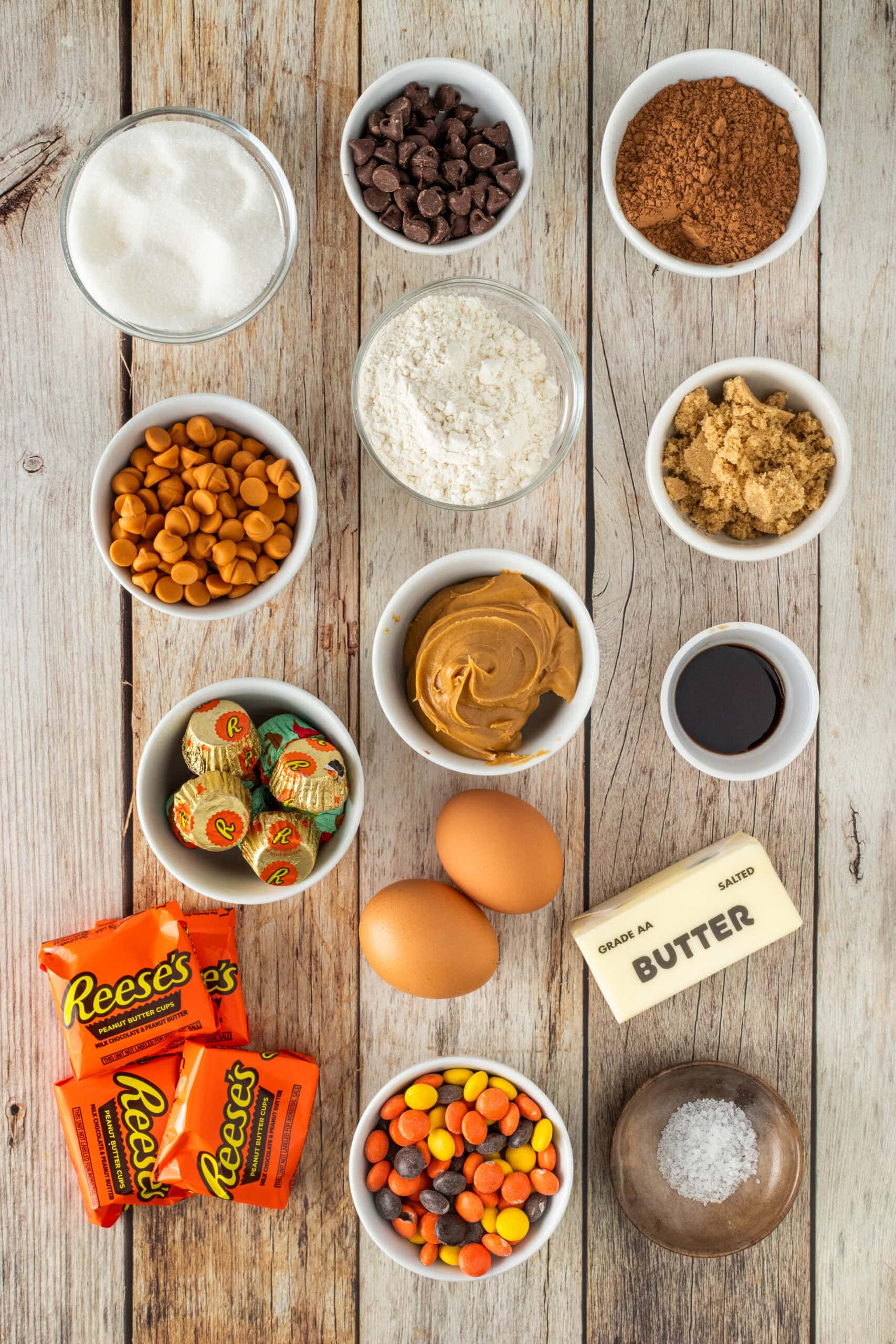 All ingredients pictured: Reese's pieces, salt, Reese's cups, eggs, butter, peanut butter, peanut butter chips, vanilla, brown and white sugar, chocolate chips, cocoa powder, flour