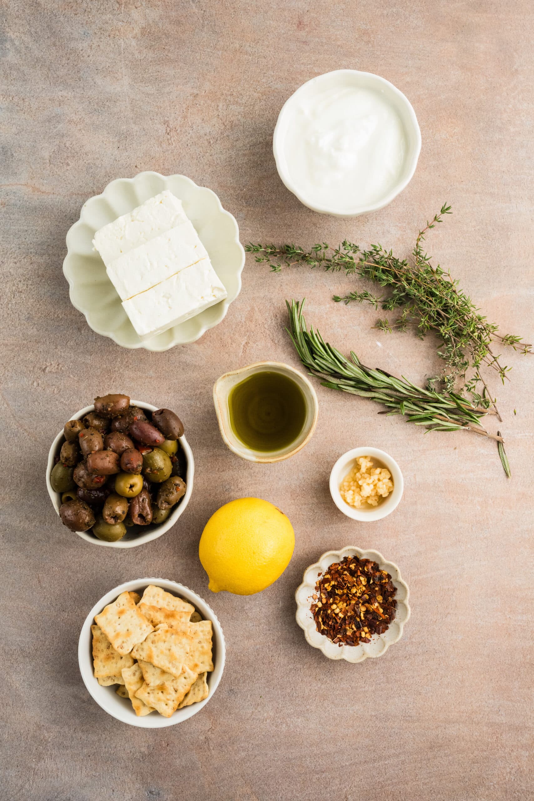 All ingredients pictured: red pepper flakes, crackers, lemon juice, garlic, olive oil, olives rosemary, thyme, feta, greek yogurt