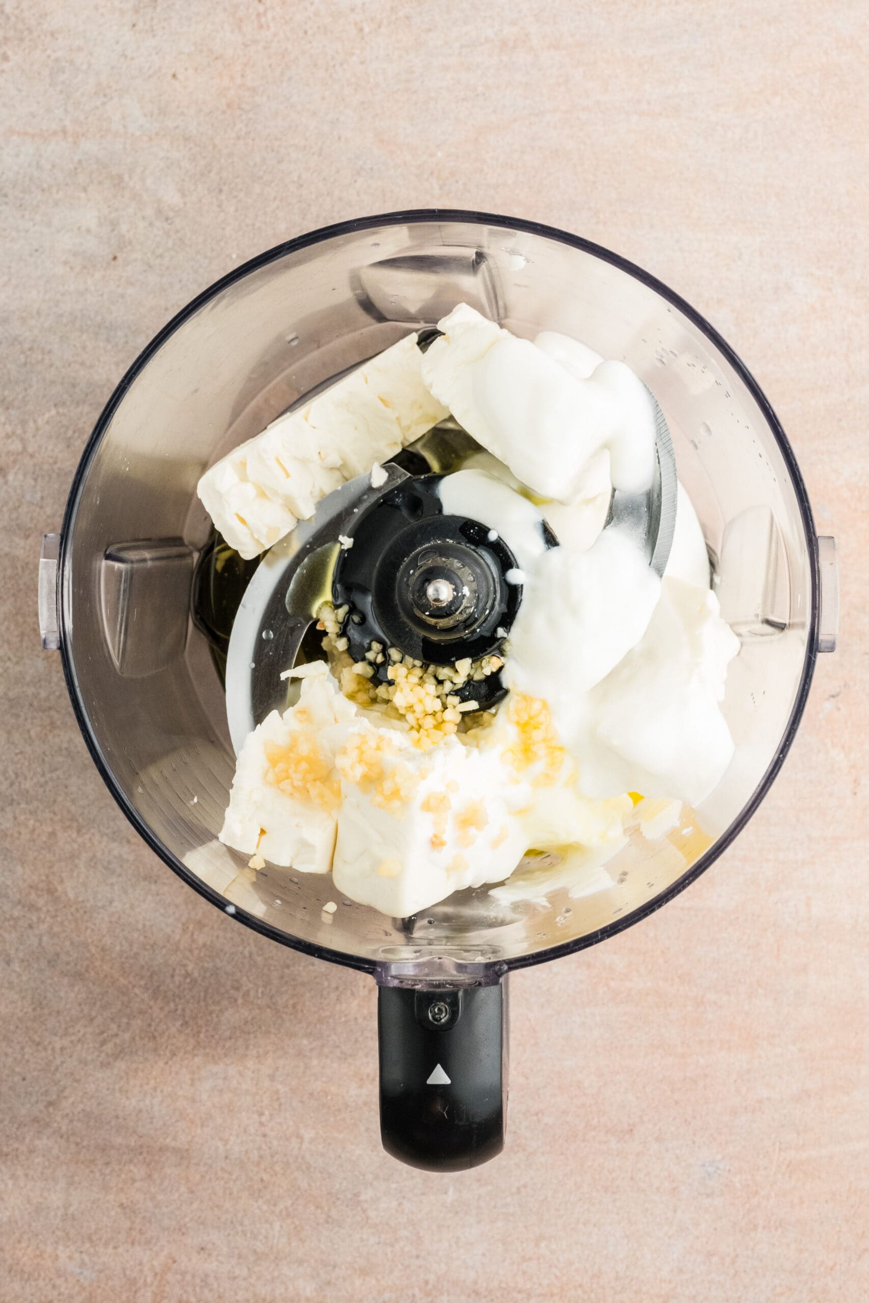In a food processor is starting the process of whipping the feta. There is also greek yogurt, olive oil, lemon juice and garlic in the processor.