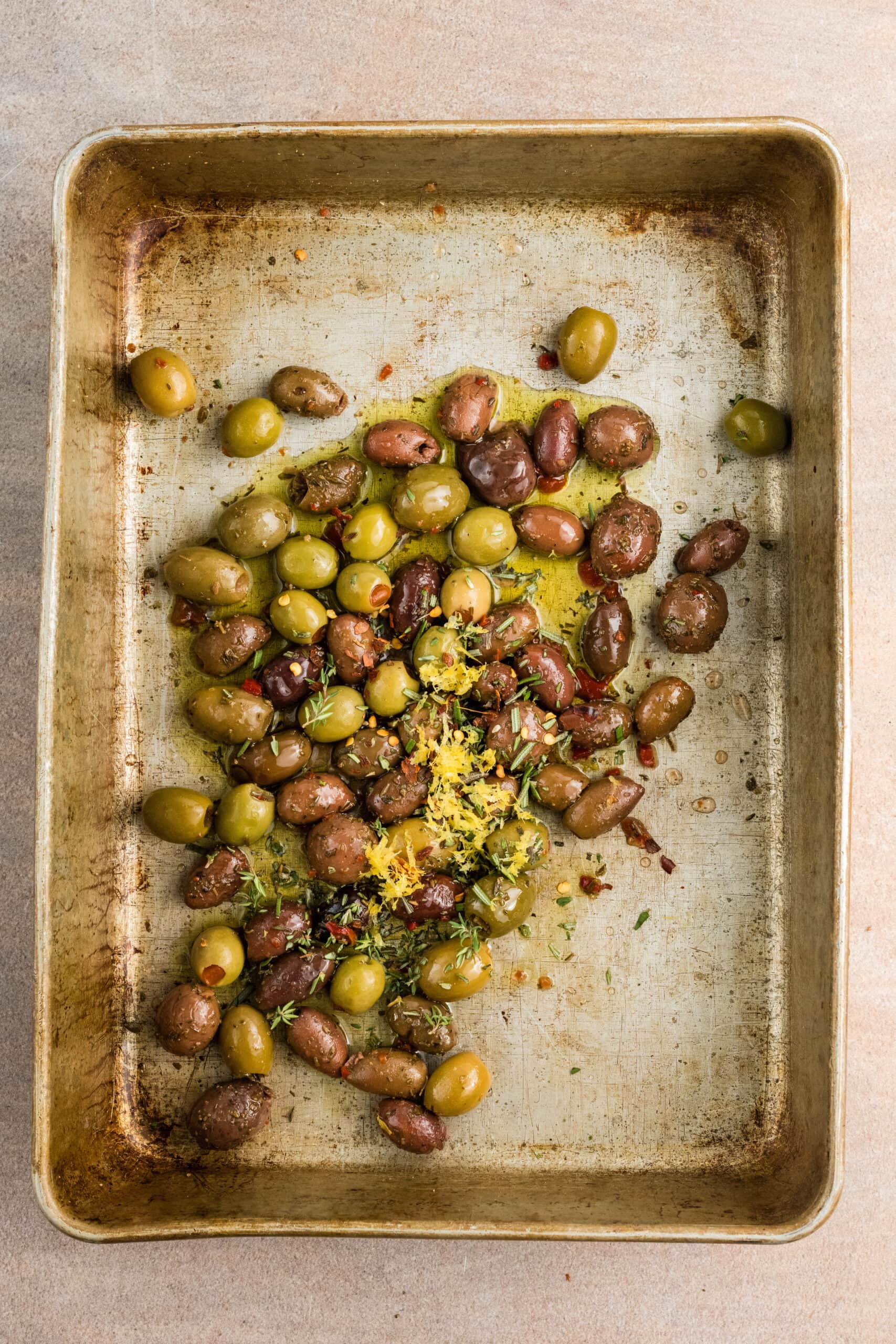 Olives with oil, thyme, rosemary, lemon zest, and red pepper flakes on a baking dish
