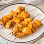 a close up of air fryer buffalo chicken thighs on skewers on a white plate