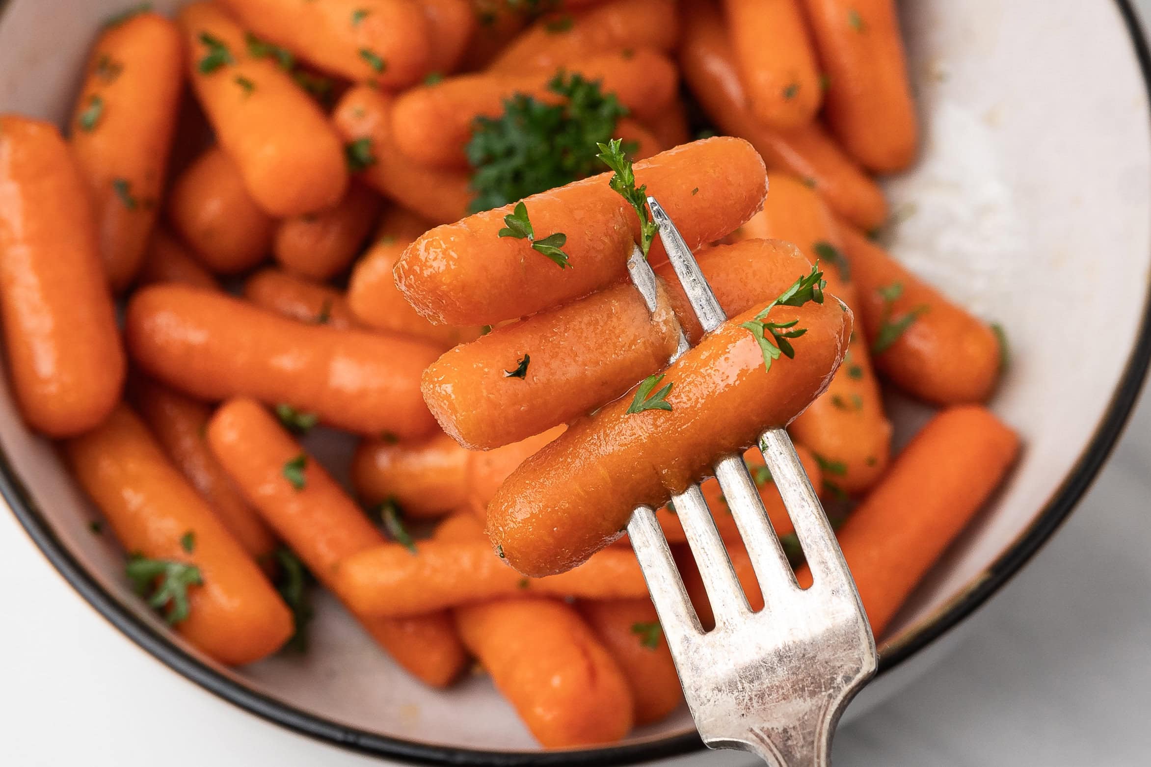 A fork holding up 3 baby carrots with parsley