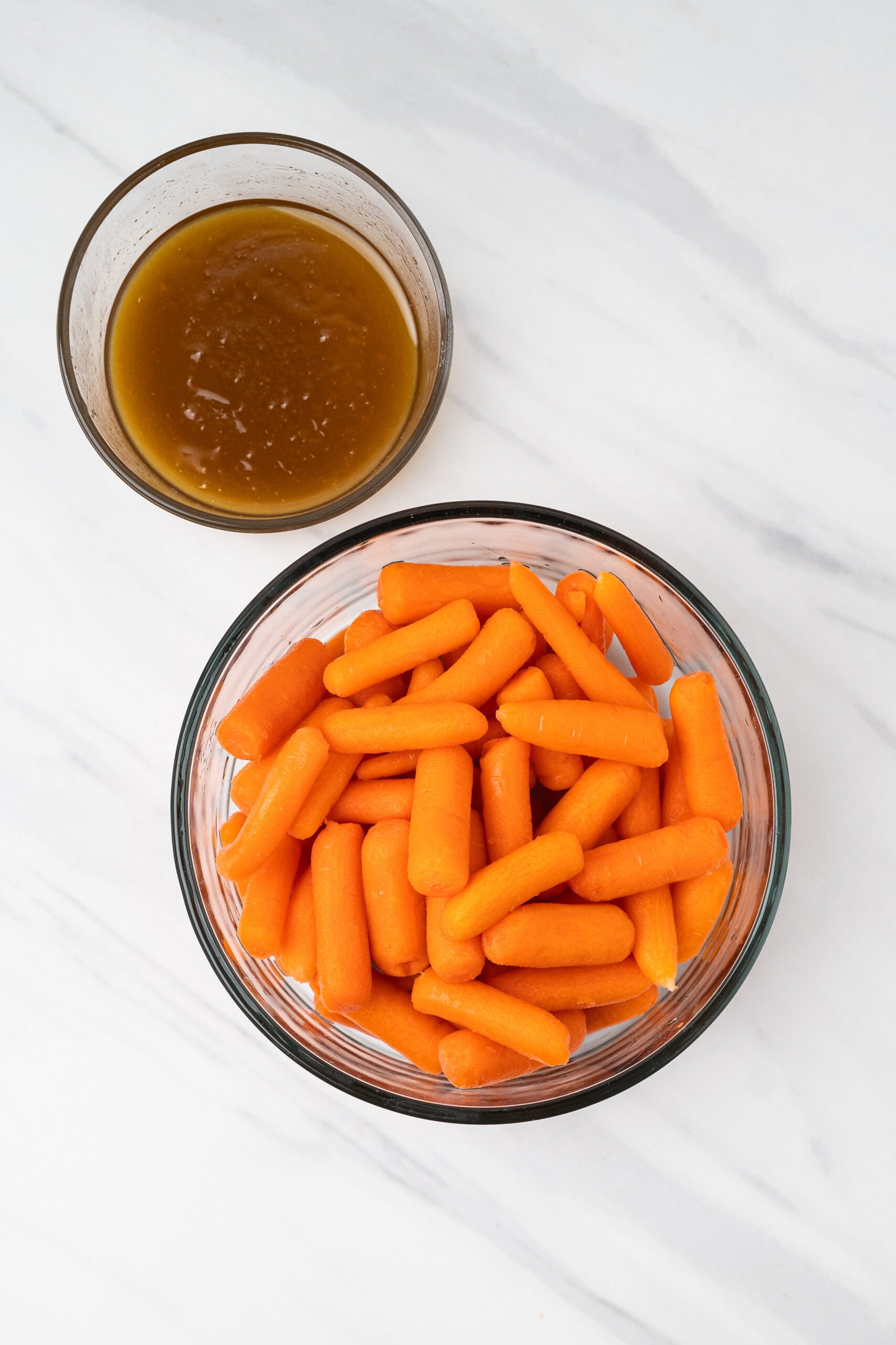 Baby carrots in a glass bowl, next to it is the glaze for the carrots