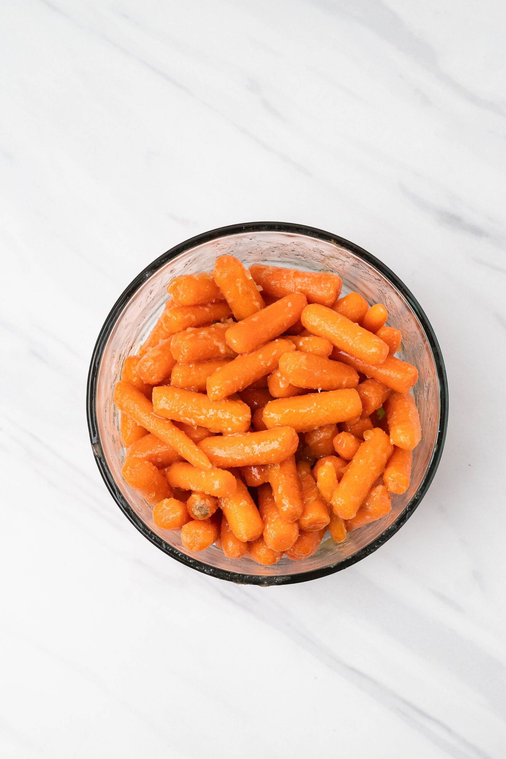 Baby carrots coated in melted butter, brown sugar, honey, olive oil in a glass bowl