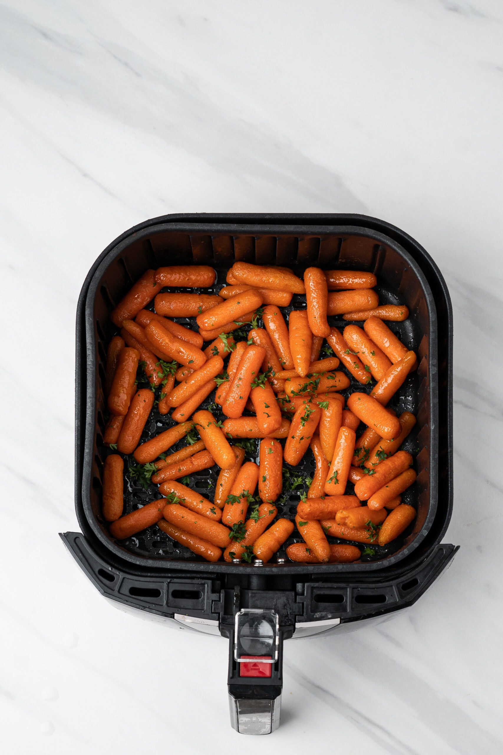 Air Fryer baby carrots are all cooked and being cooled in the air fryer with fresh parsley on top