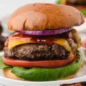 a close up of an air fryer ground turkey burger loaded up with cheddar cheese, red onion, sliced tomato, leaf lettuce, and ketchup on a tall bun
