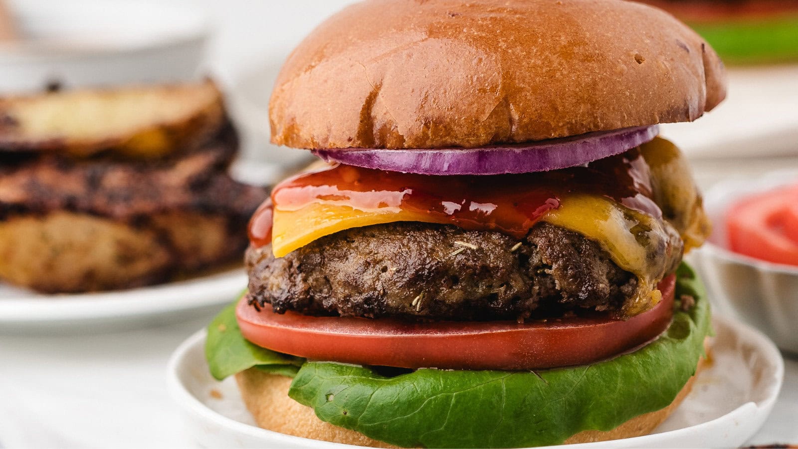 an air fryer ground turkey burger loaded up with cheddar cheese, red onion, sliced tomato, leaf lettuce, and ketchup on a tall bun