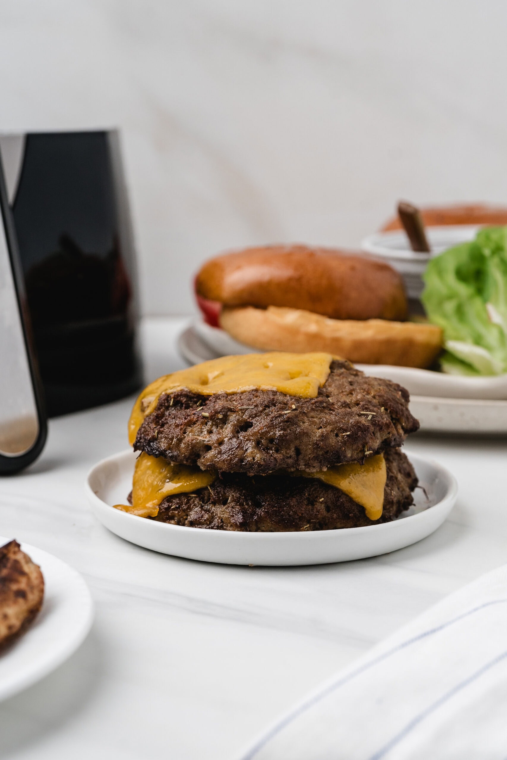 Ground turkey burgers are cooked and stacked on a small plate with melted cheese, ready to add a bun and toppings