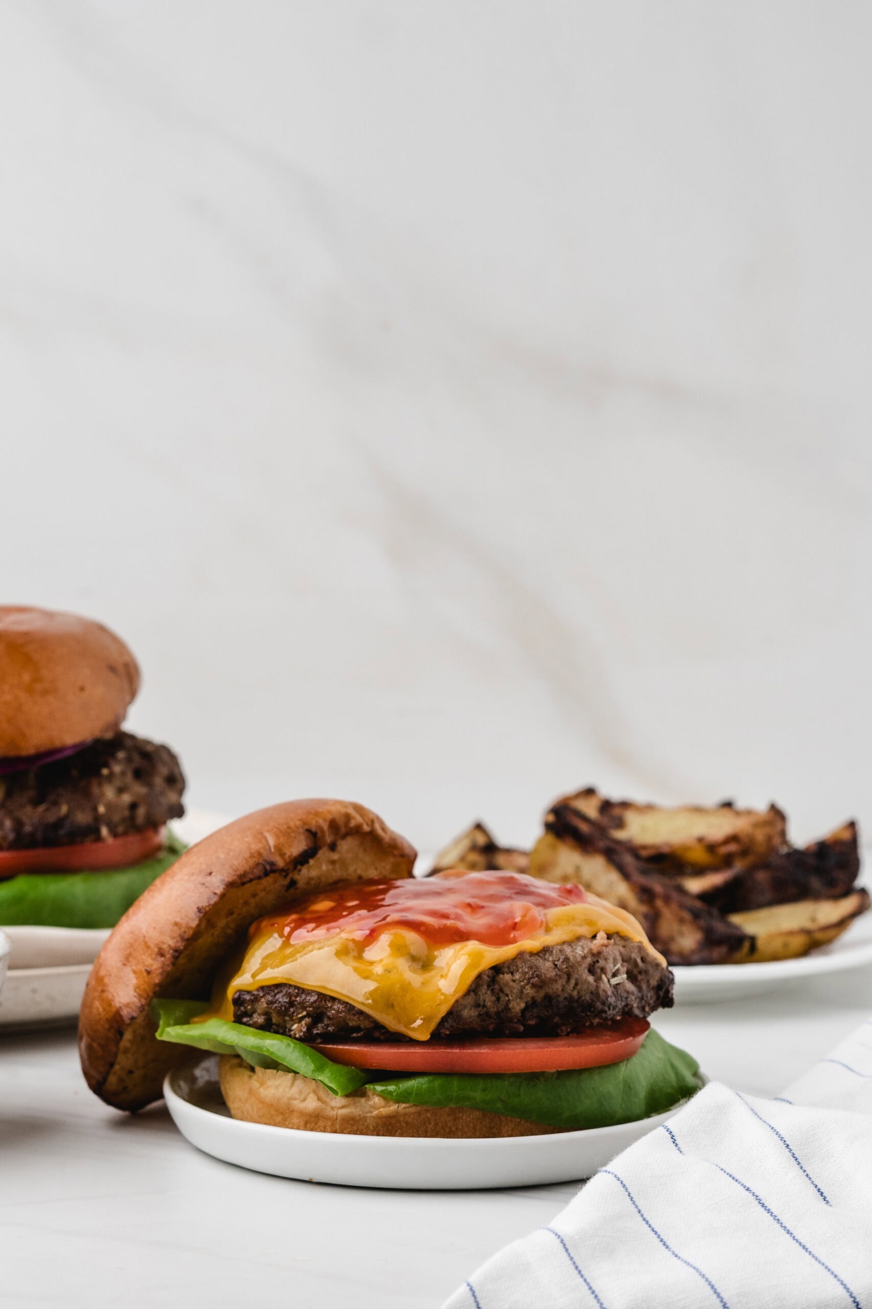 Turkey burger on a small plate, topped with tomato, lettuce, chili sauce, melted cheese with the top of the brioche bun to the side