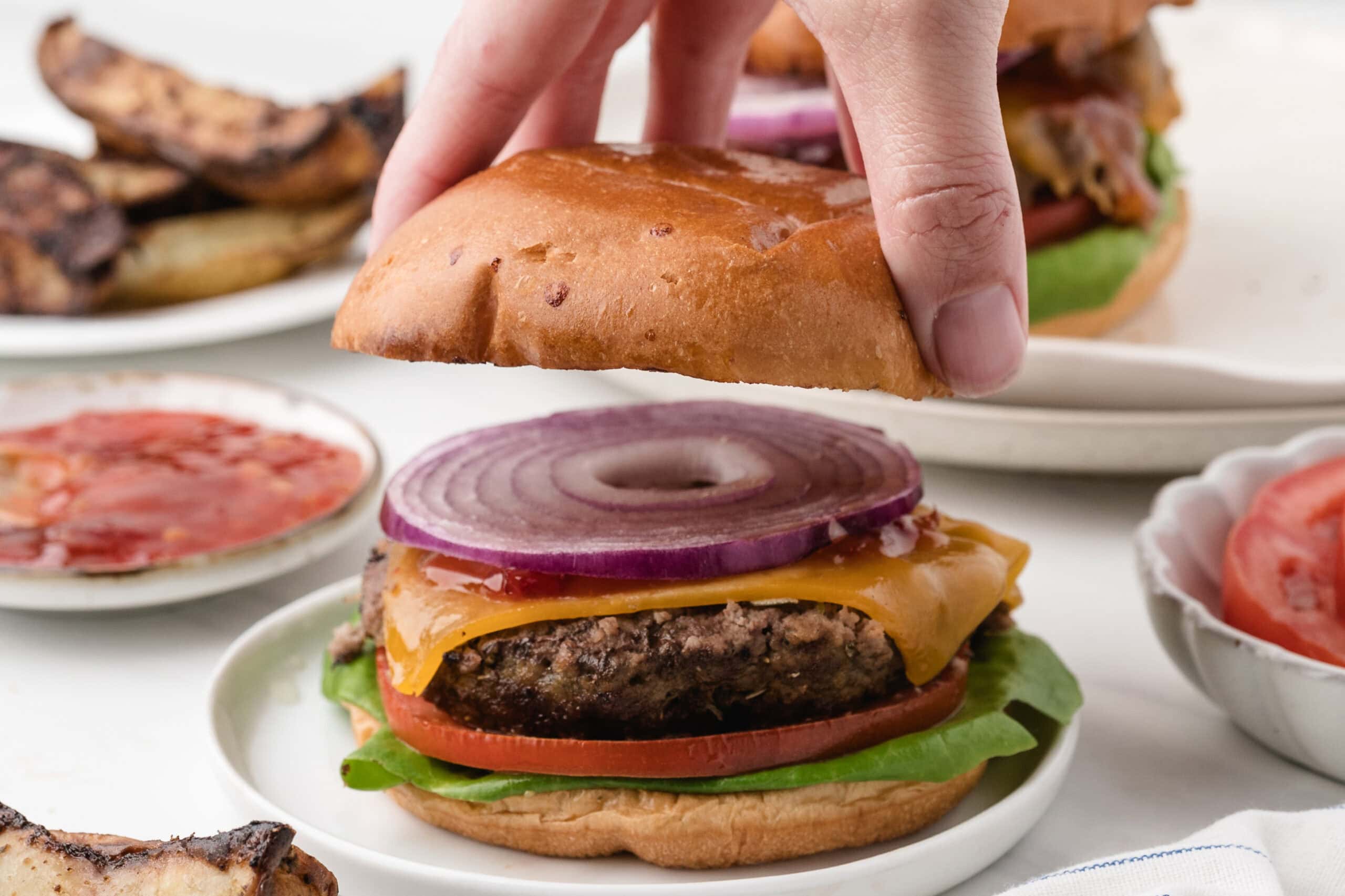 Placing the top of the brioche bun to the ground turkey burger with melted cheese, tomato slice, lettuce and chili sauce