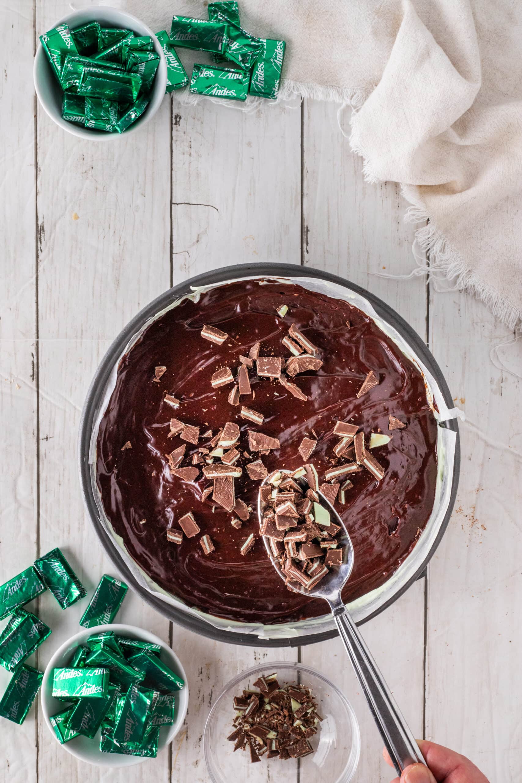 Placing Andes mint sprinkled on top of ganache layer of the cheesecake