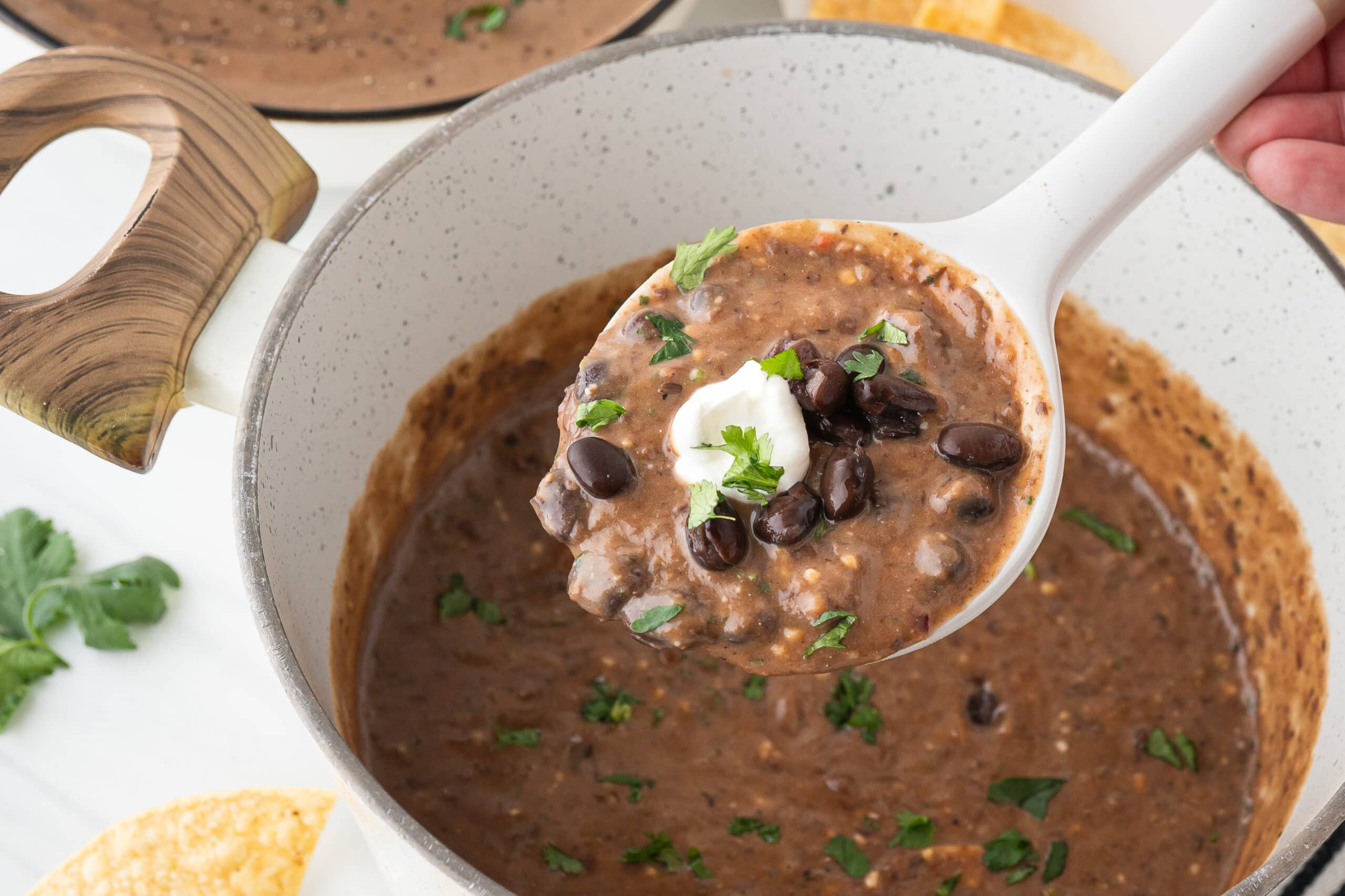 Scooping up black bean soup to be served into a bowl