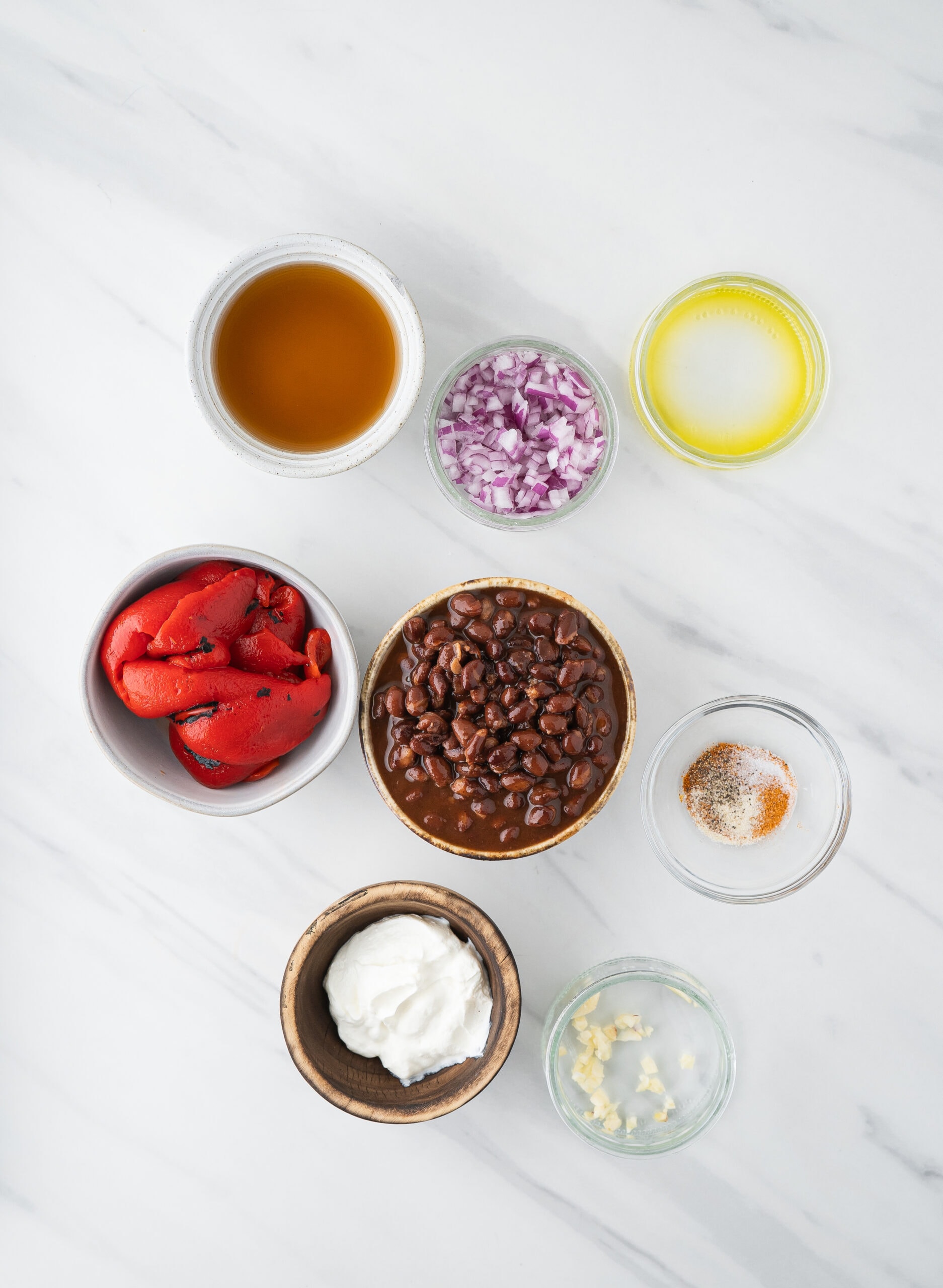 All ingredients to make black bean soup: canned black beans, garlic, chopped onion, sour cream, roasted red pepper, olive oil, cumin, oregano, salt and pepper