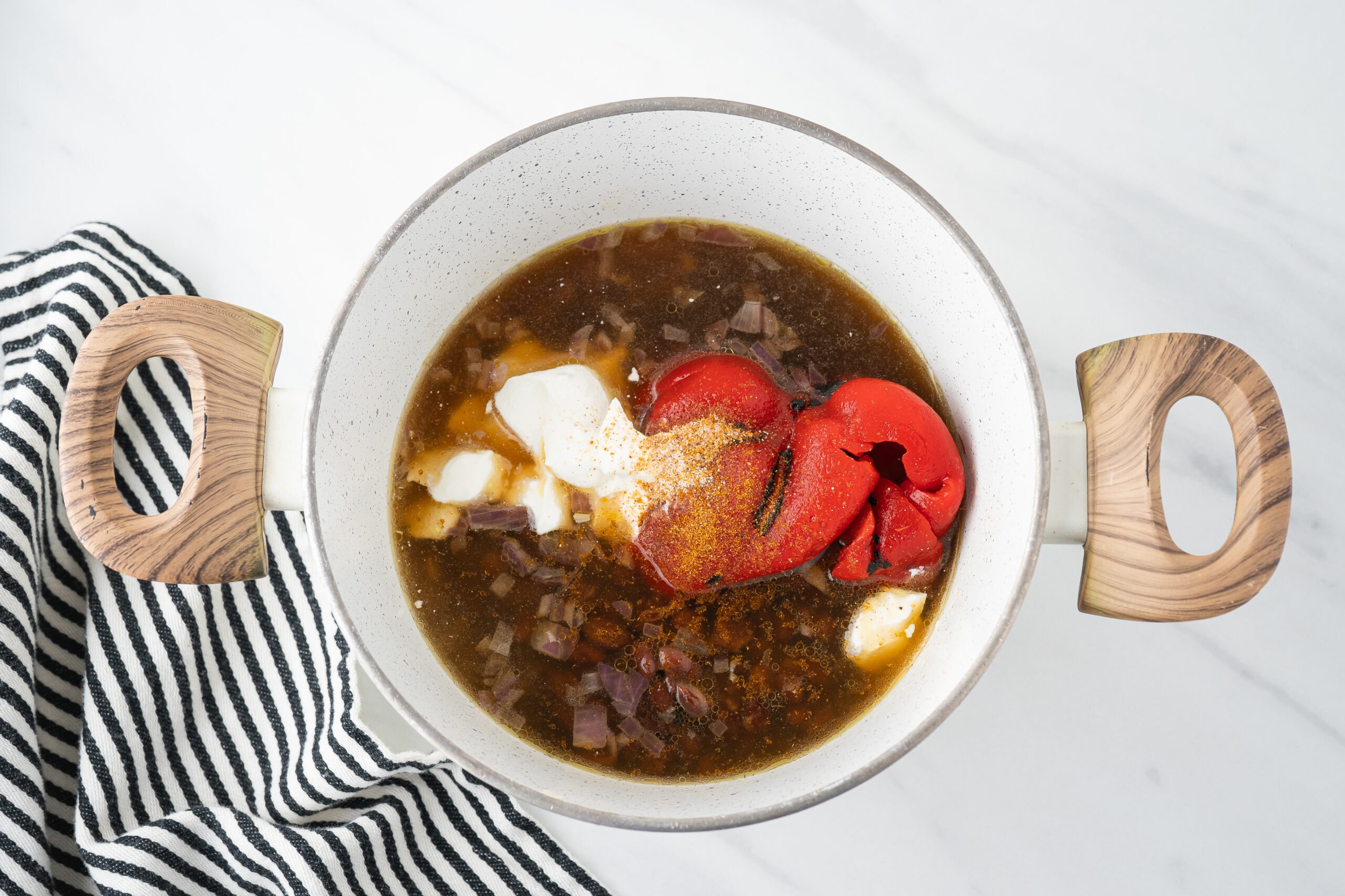 Adding sour cream, roasted red pepper, oregano, cumin and salt and pepper in the pan with the canned black beans and chicken broth