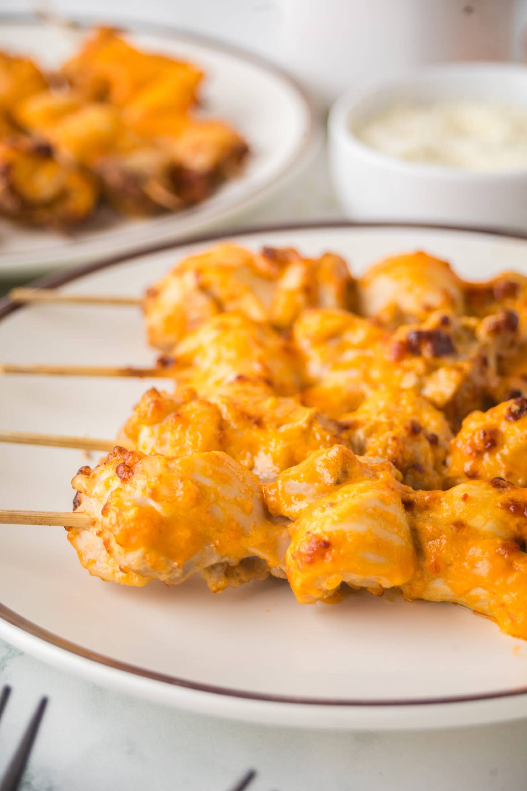 Close up of buffalo chicken thighs on a skewer with a drizzle of buffalo sauce and parmesan