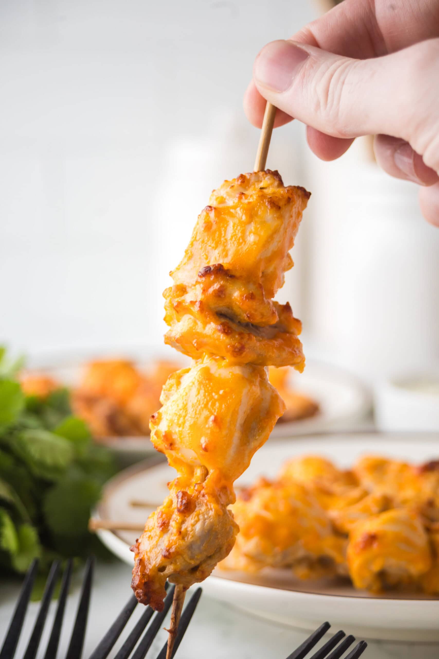 Air fryer buffalo chicken thighs being held up with a skewer, showing it's texture to the side