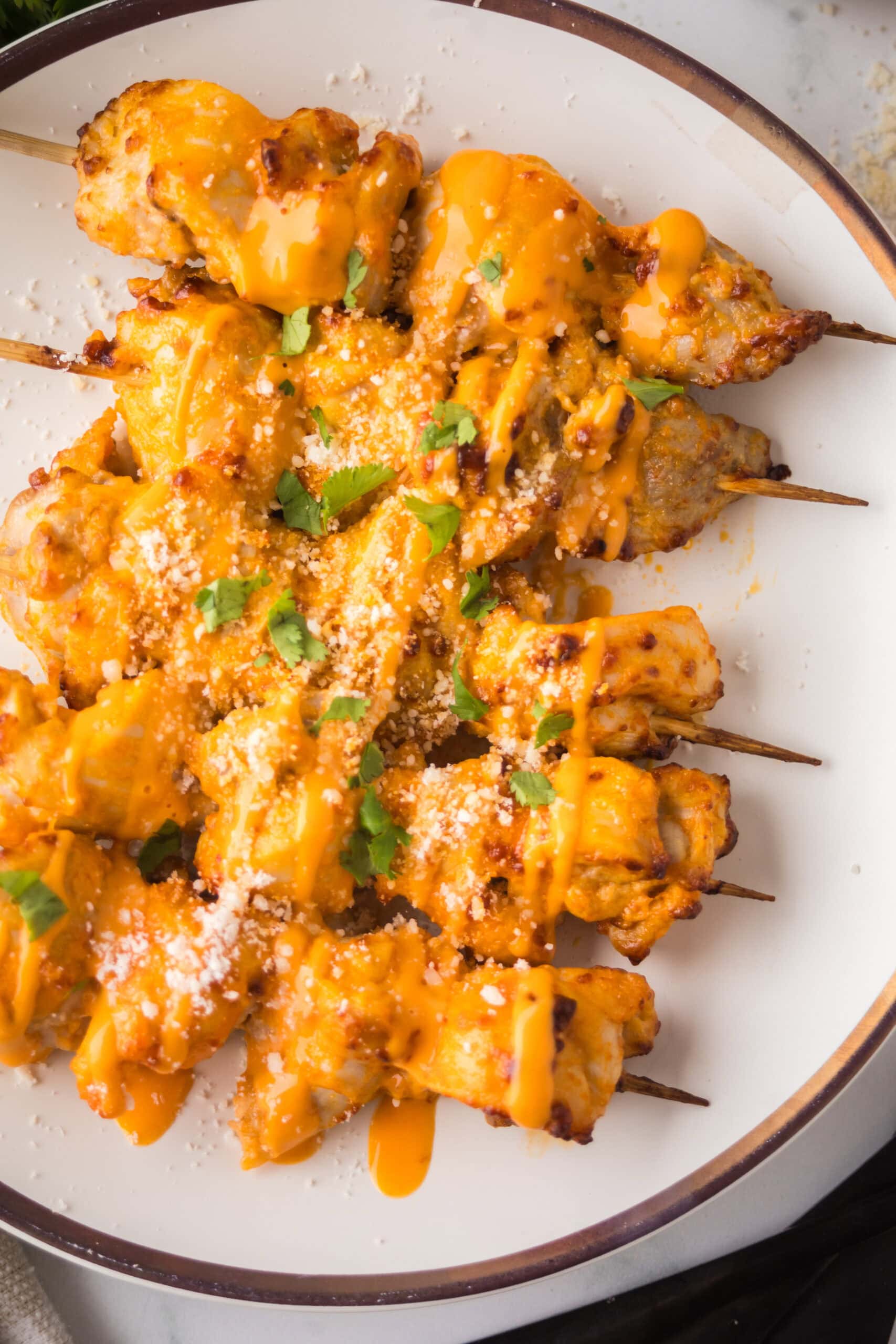 Buffalo chicken thighs on a plate, topped with more parmesan cheese and drizzled with buffalo sauce